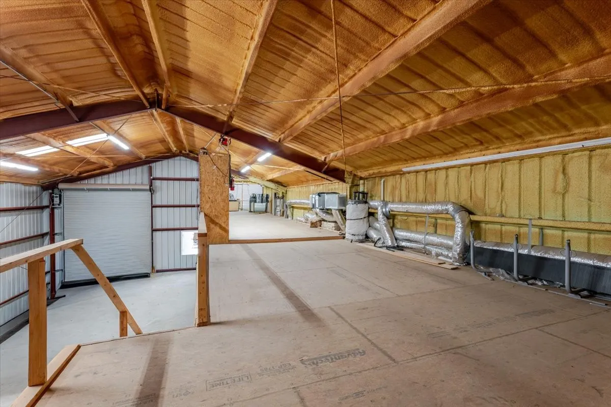 Spacious open-concept interior featuring vaulted ceilings with exposed steel beams, high-density spray foam insulation, an integrated mezzanine level, and industrial LED lighting