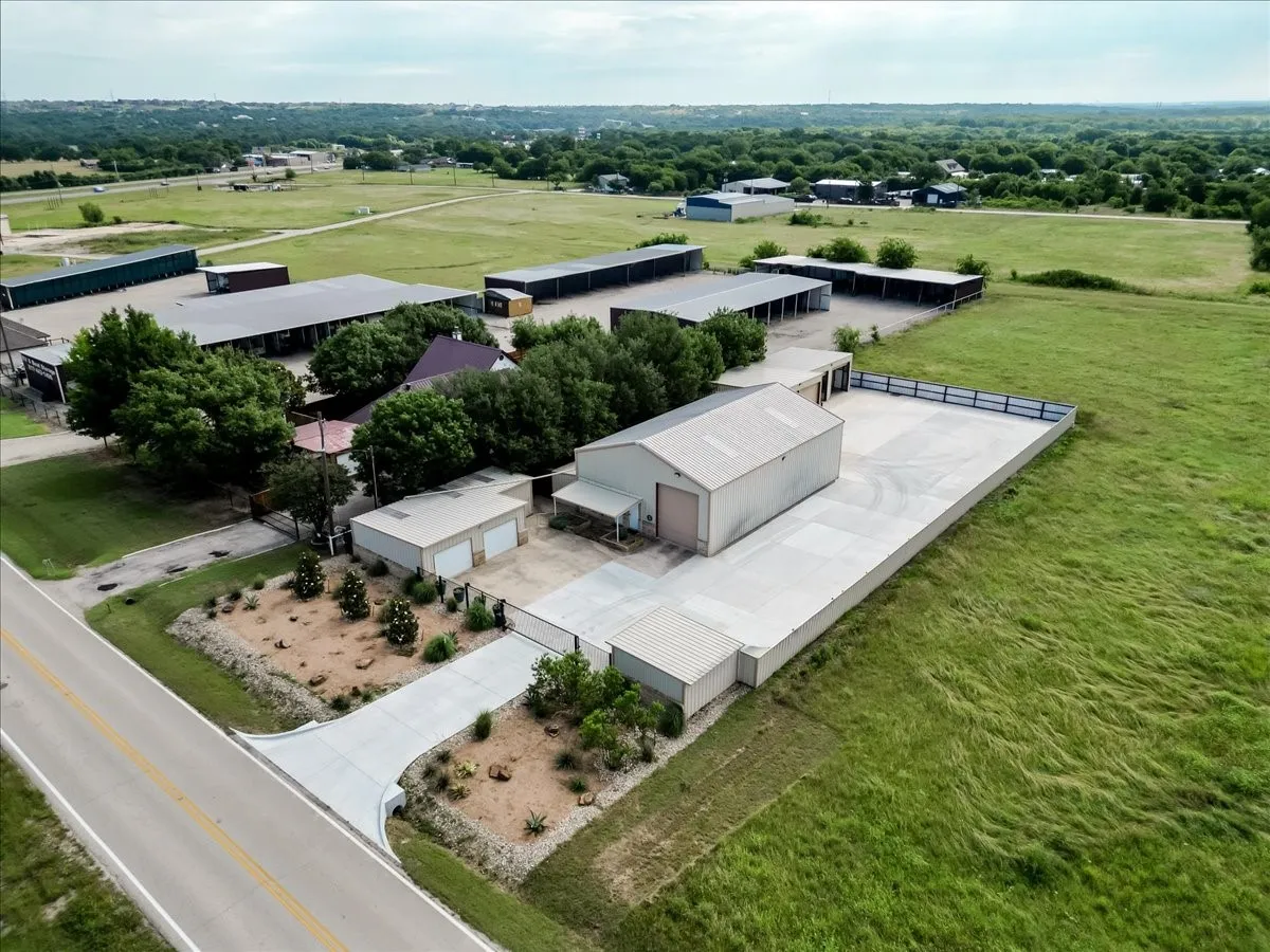Property featuring multiple metal-siding storage structures, fenced perimeter, extensive concrete paving, and landscaped xeriscaping