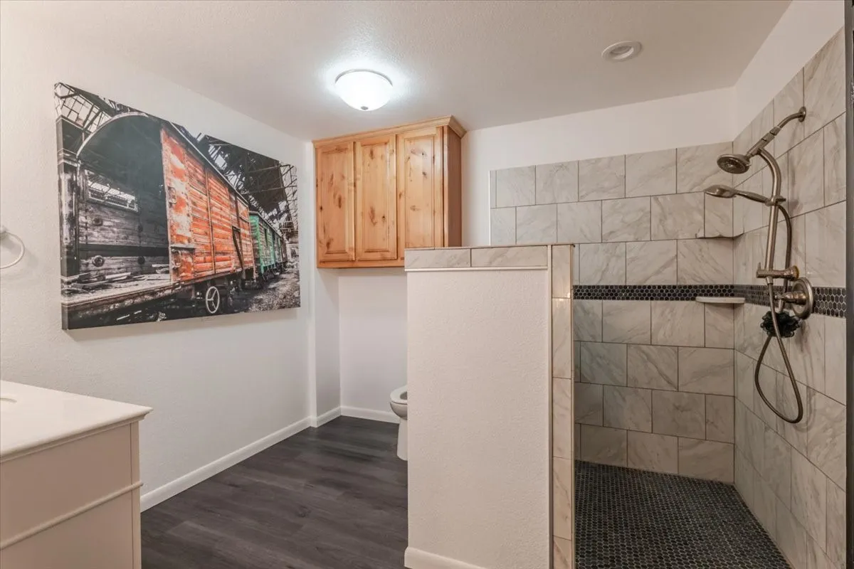 Bathroom featuring wood-finish flooring, a wall-mounted wood cabinet, and a walk-in shower with tiled walls, a tiled floor, and a metal shower fixture