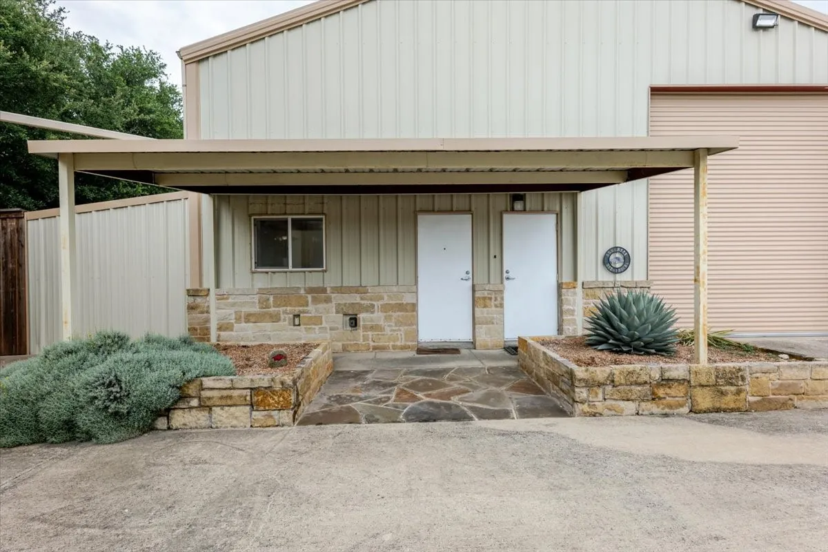 Metal-clad exterior featuring a covered entryway, natural stone masonry facade, flagstone paving, and raised stone planter beds