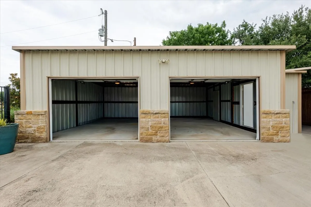Detached two-car garage featuring metal siding, stone masonry accents, a concrete driveway, and interior wall-mounted​​‌​​​​‌​​‌‌​‌‌​​​‌‌​‌​‌​‌​​​‌​​ lighting