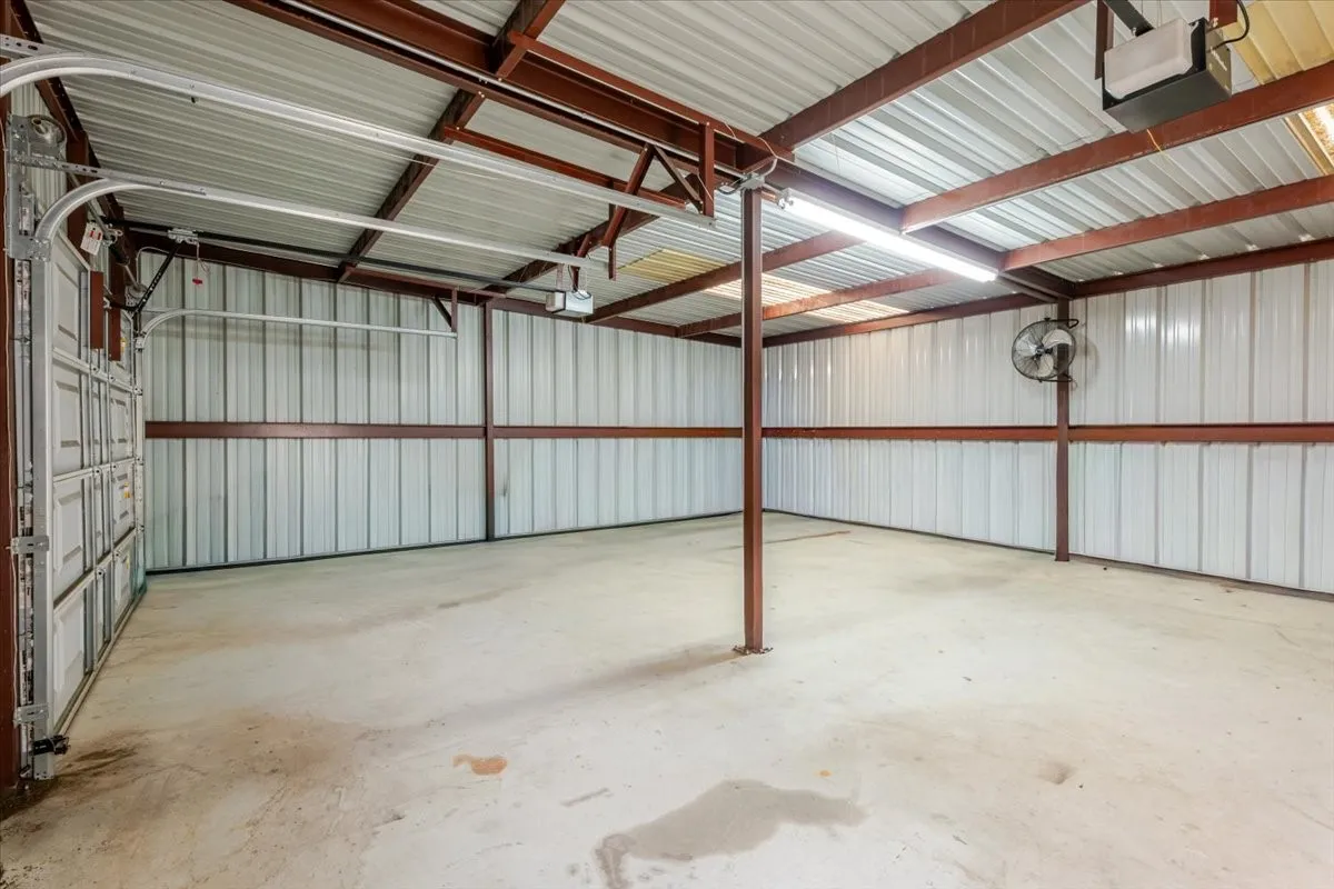 Garage space featuring metal wall paneling, structural steel framing, concrete flooring, dual automatic door openers, and overhead lighting