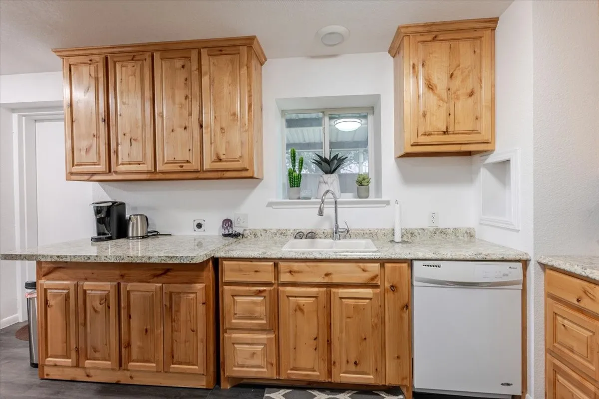 Breakroom - Knotty wood cabinetry, light-toned stone-finish countertops, white double-basin sink, high-arc faucet, and built-in dishwasher
