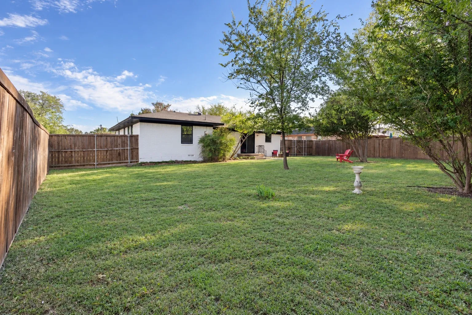 Expansive backyard featuring a manicured lawn, perimeter wood fencing, and mature trees