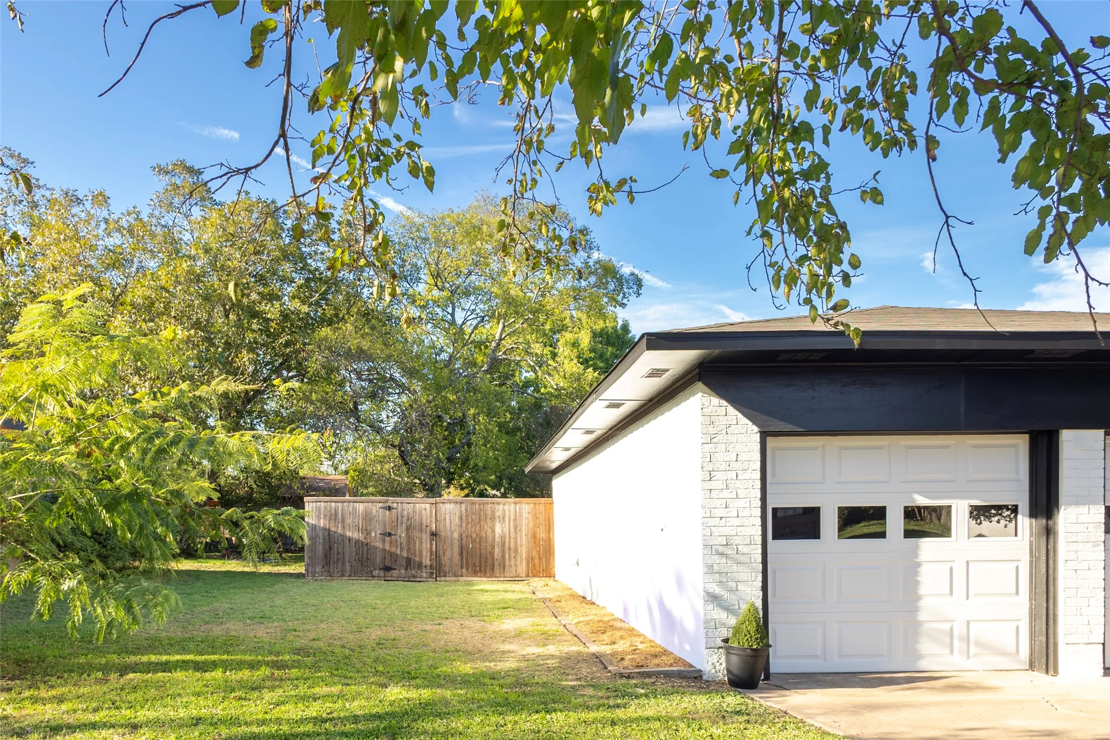 White brick exterior with black trim, detached garage featuring a multi-panel door with glass inserts, and a fenced yard with mature trees