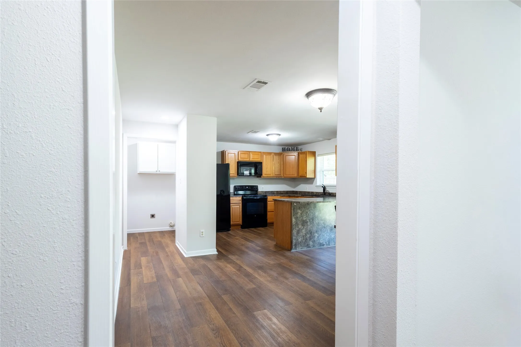 Kitchen featuring wood-finish cabinetry, stone-texture countertops, black appliances, and wood-finish flooring