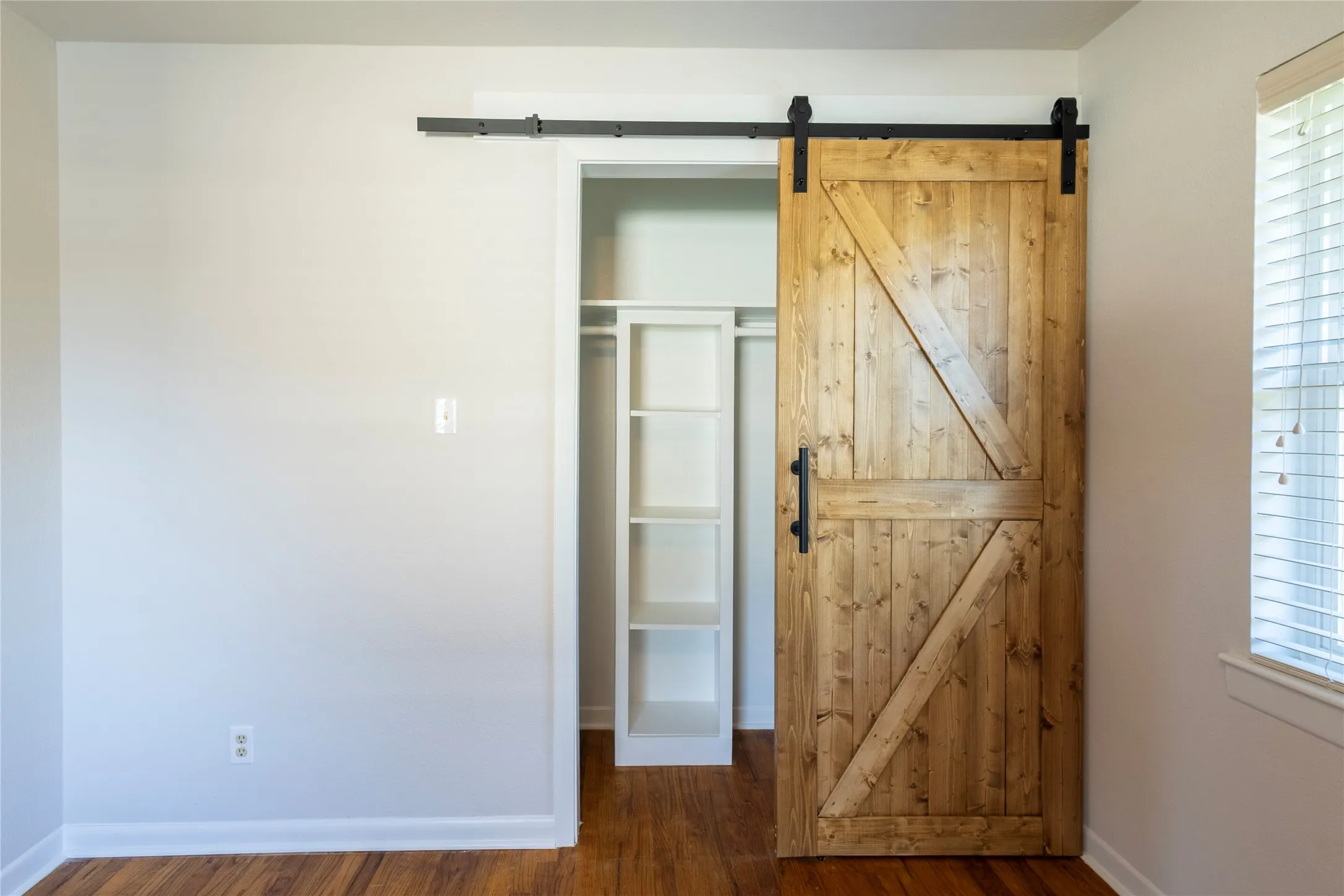 Sliding wood-finish barn door with black hardware, built-in closet shelving, and wood-finish flooring