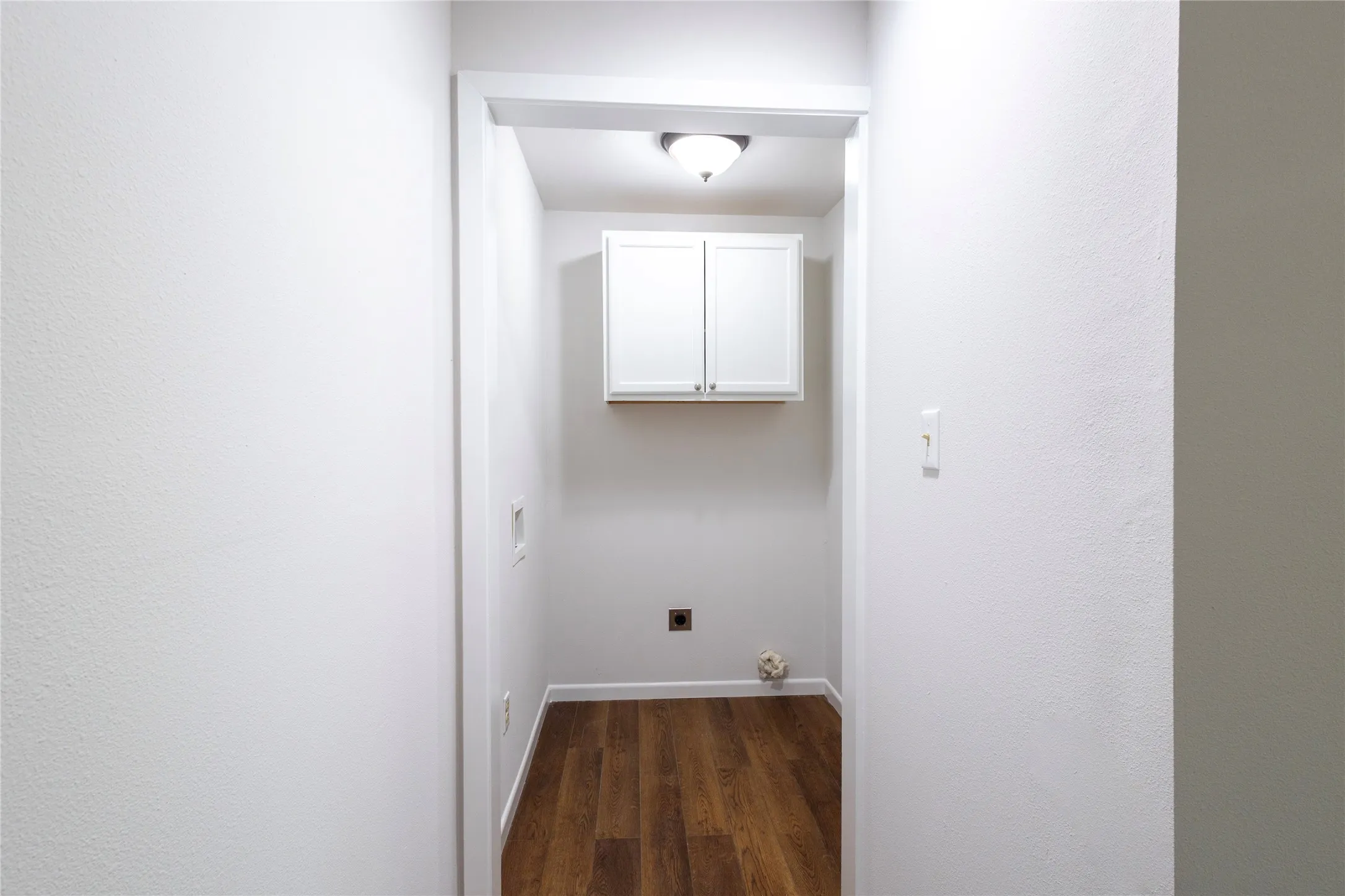 Utility space featuring wood-finish flooring, white wall-mounted cabinetry, and a ceiling-mounted light fixture