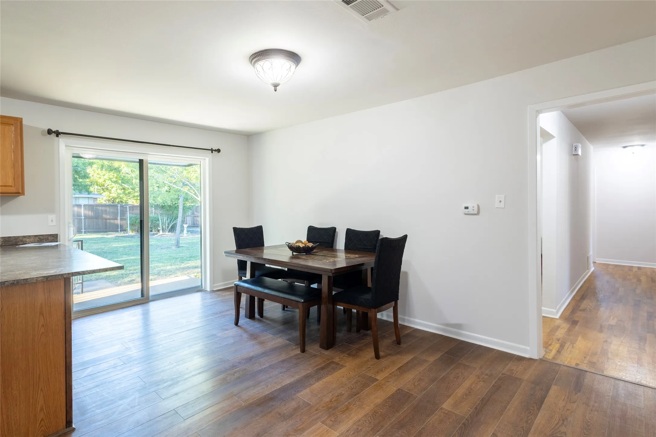 Wood-finish flooring, sliding glass door, flush-mount ceiling light fixture, and kitchen counter overhang