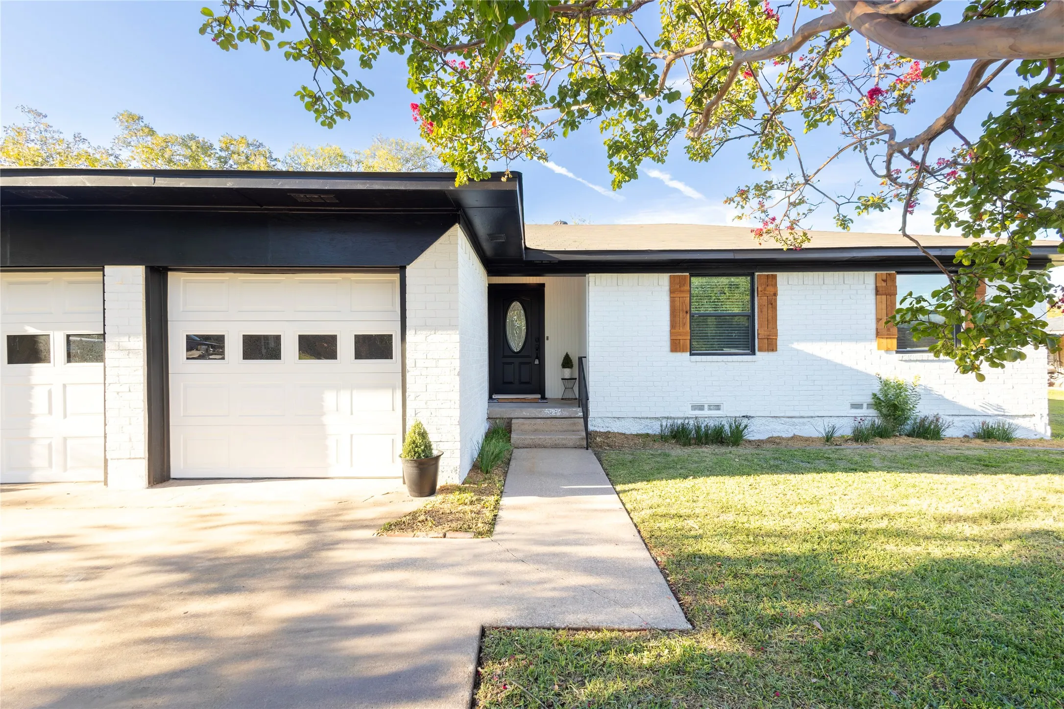 Single-story residence featuring a painted brick exterior, dual-car garage, recessed entryway with a solid-panel door, and decorative wood-finish window shutters