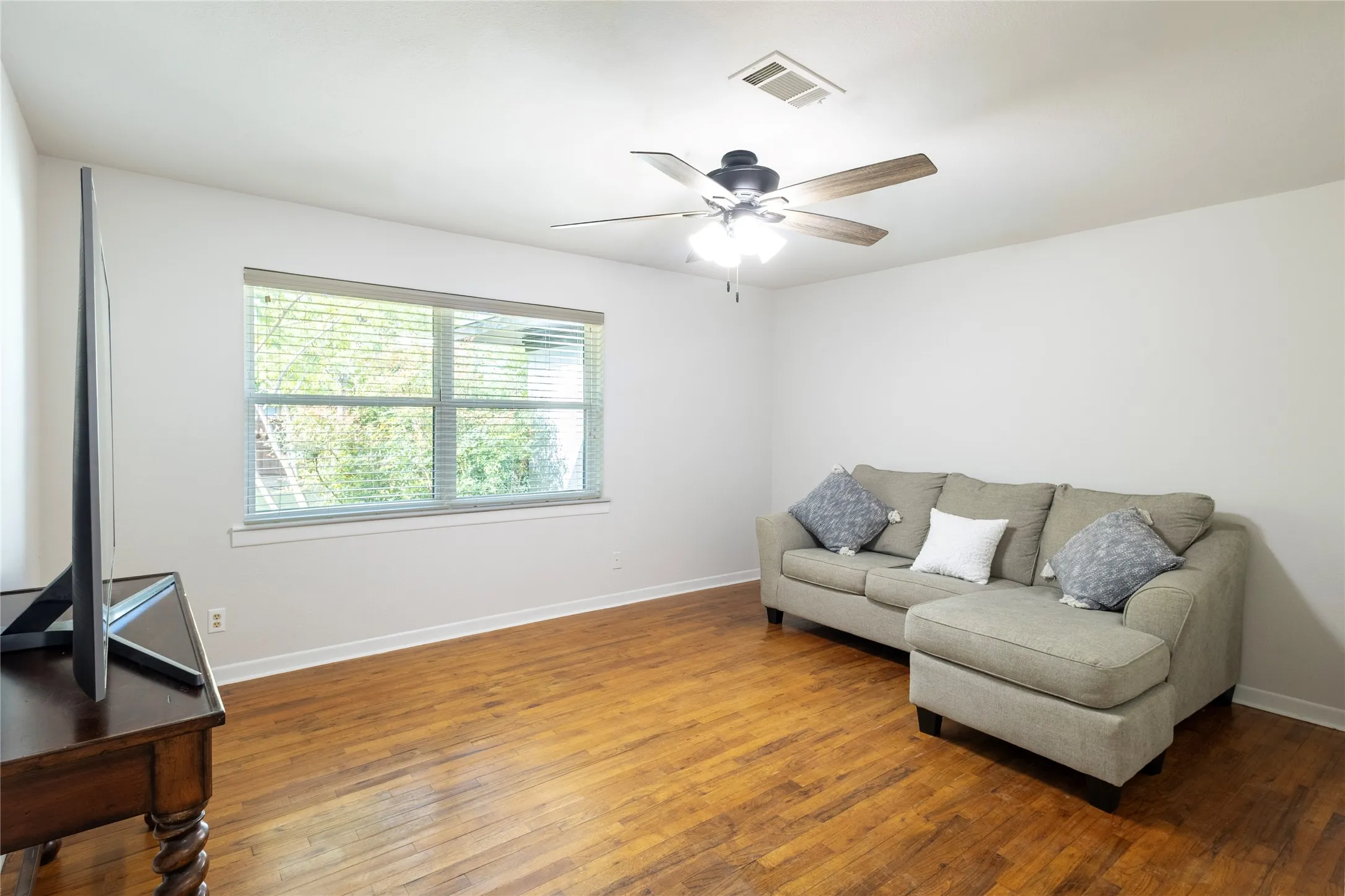 Room featuring wood-finish flooring, a ceiling fan with integrated lighting, and a window with blinds