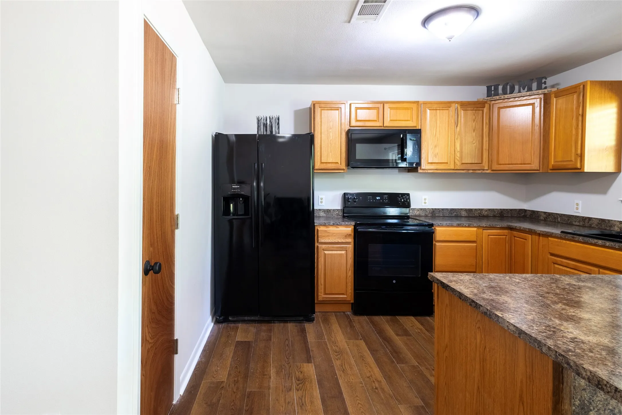Kitchen featuring wood cabinetry, dark laminate countertops, wood-finish flooring, and black appliances including a built-in microwave and range