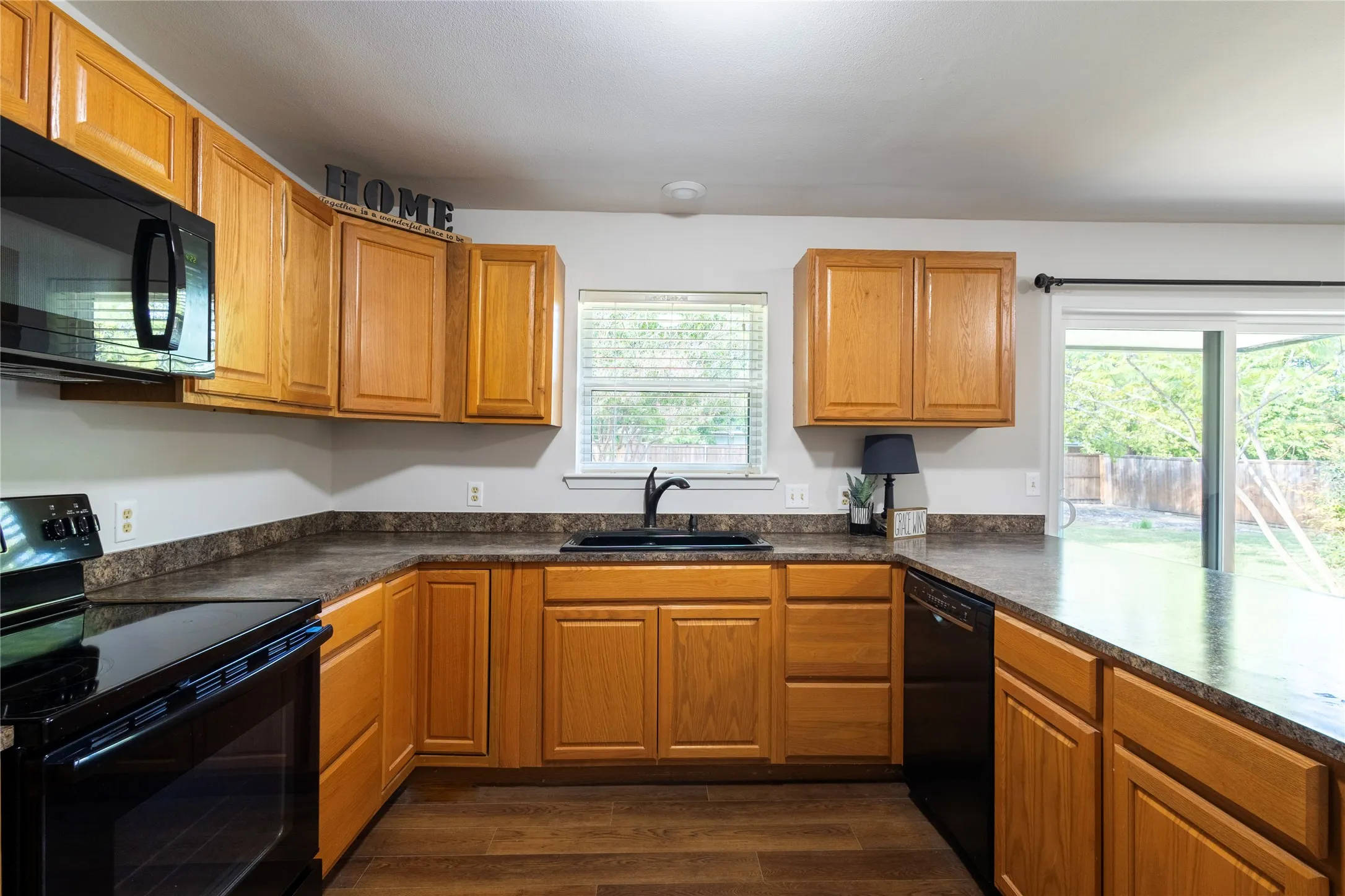 Kitchen featuring stained wood cabinetry, stone-patterned laminate countertops, wood-finish flooring, integrated black appliances, and sliding glass doors