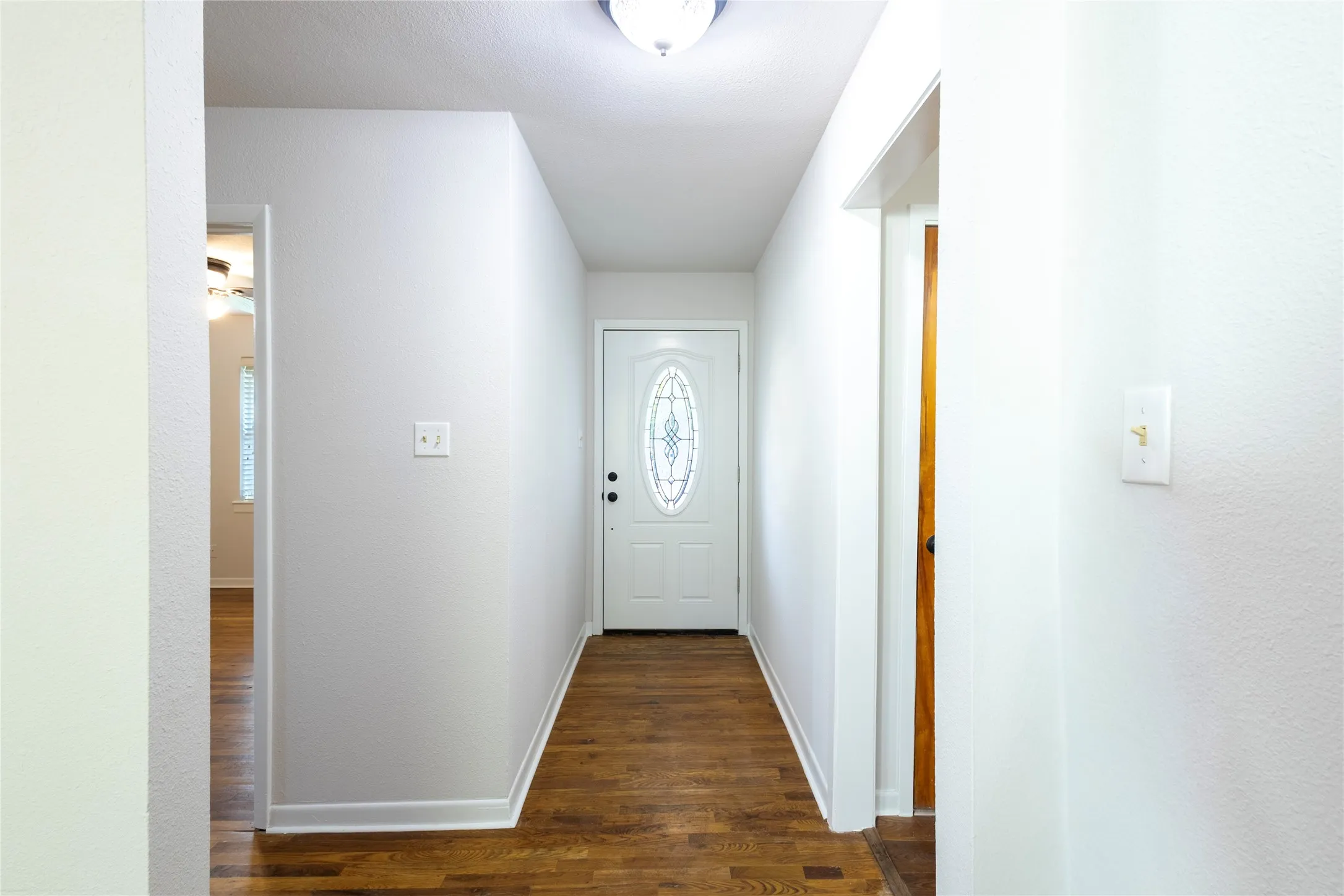Entryway featuring wood-finish flooring, a white door with an oval decorative glass insert, and a flush-mount ceiling light fixture