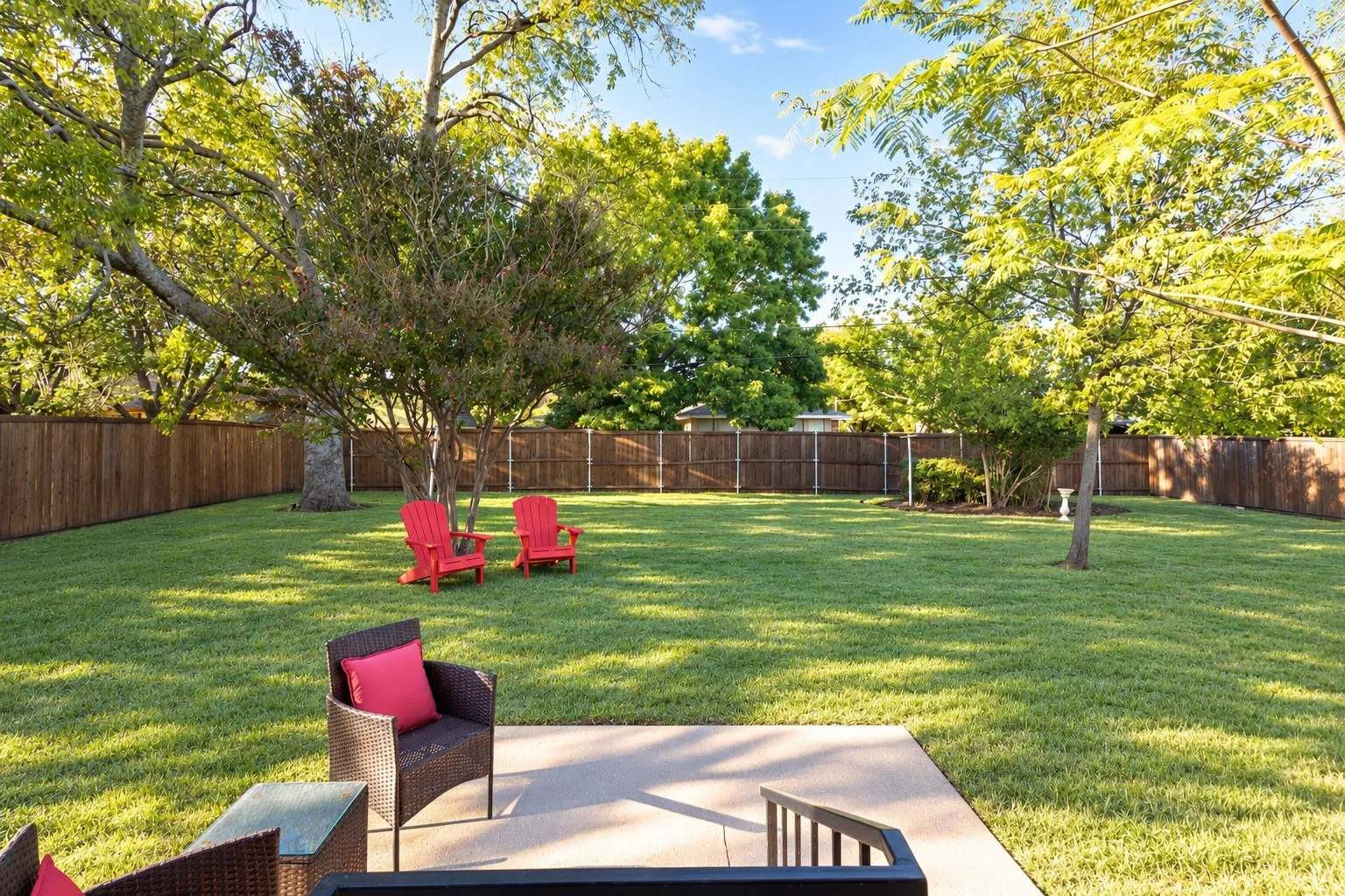 Expansive backyard featuring a concrete patio, wood privacy fencing, and mature trees