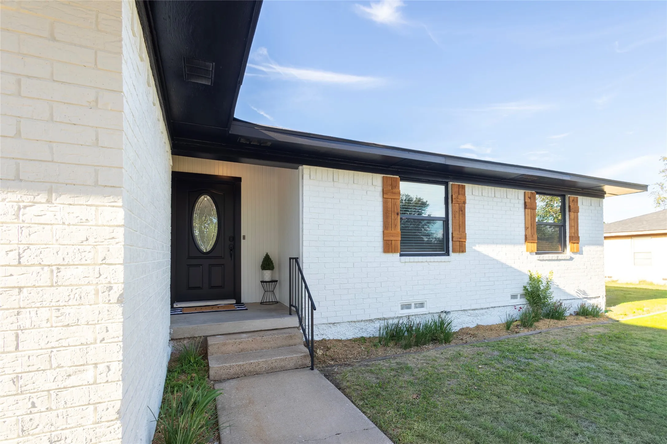 Exterior facade featuring painted brick, dark trim, decorative wood shutters, and an entryway door with an oval glass insert