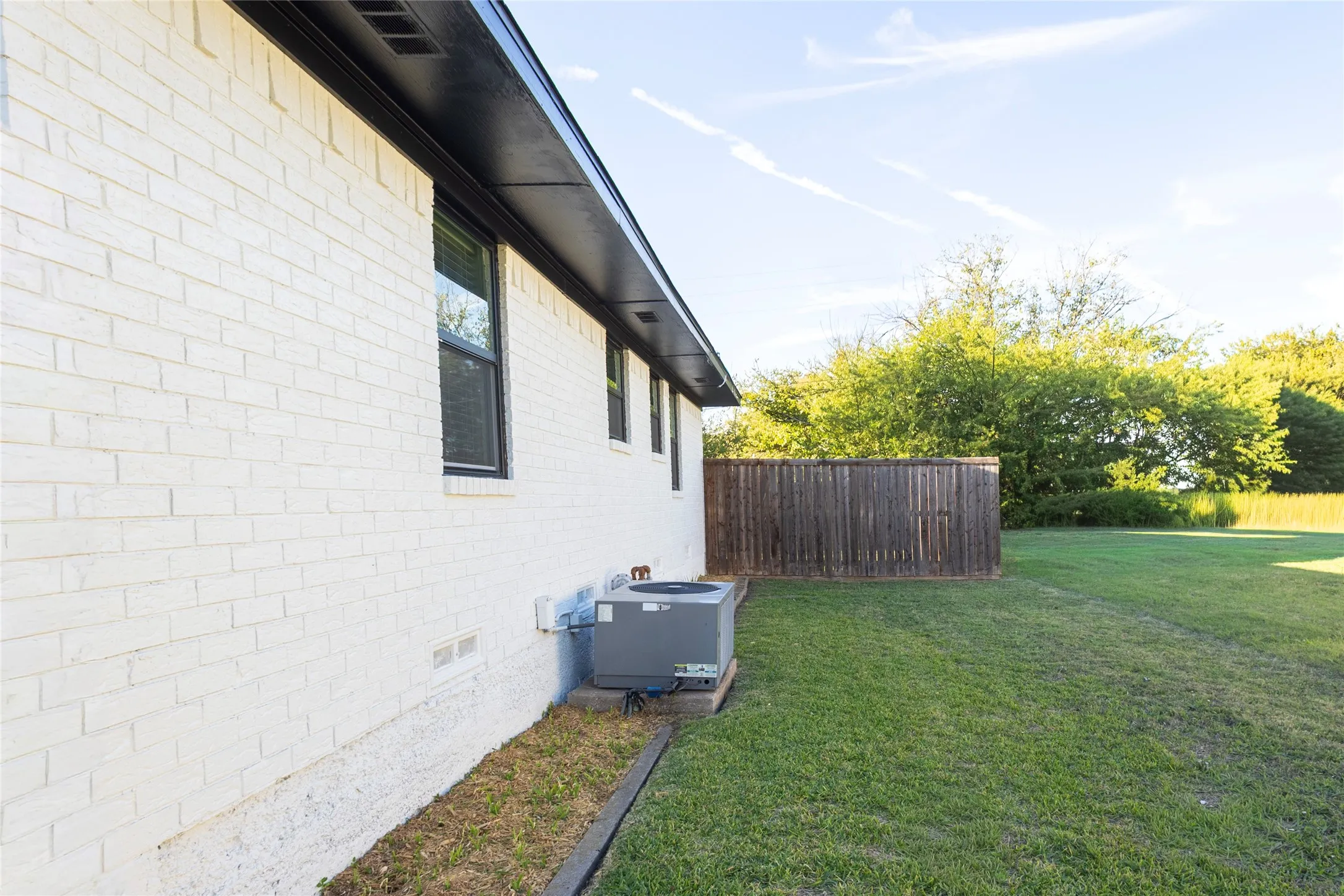 Painted brick exterior with dark trim, expansive lawn, and wood privacy fencing