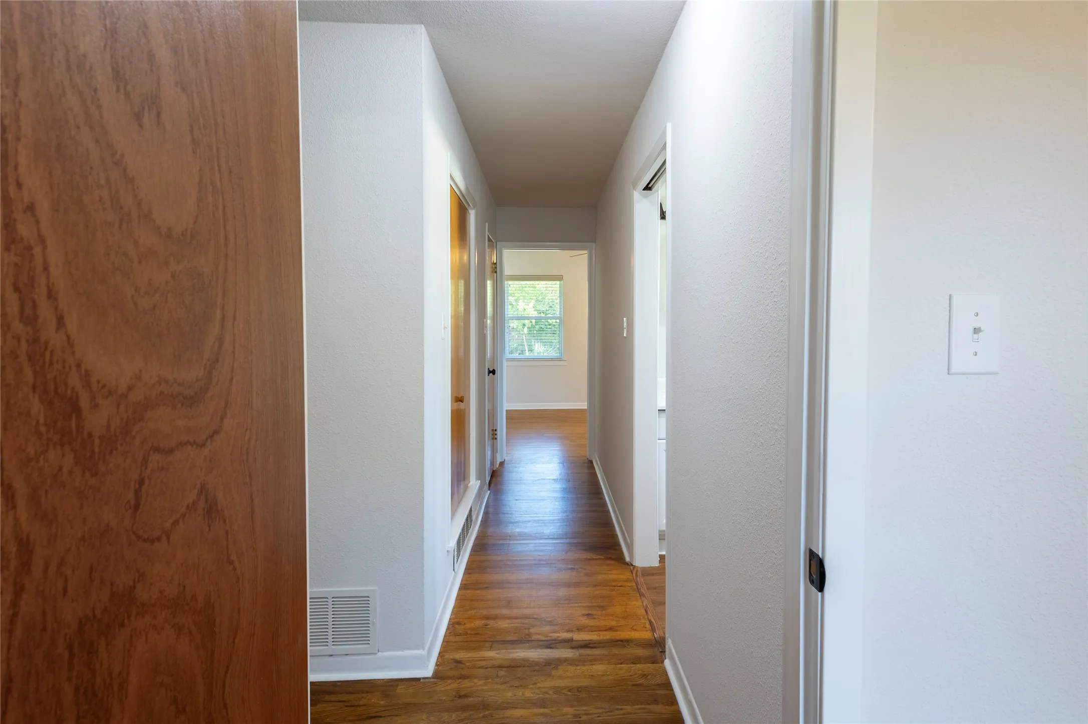 Hallway featuring wood-finish flooring, smooth-finish walls, and wood-grain interior doors