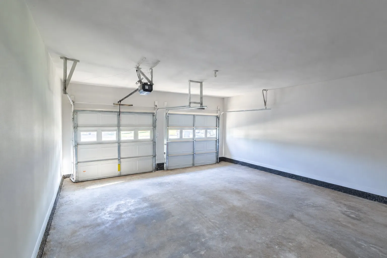 Two-car garage featuring finished walls, concrete flooring, and two automated sectional garage doors with paneled windows