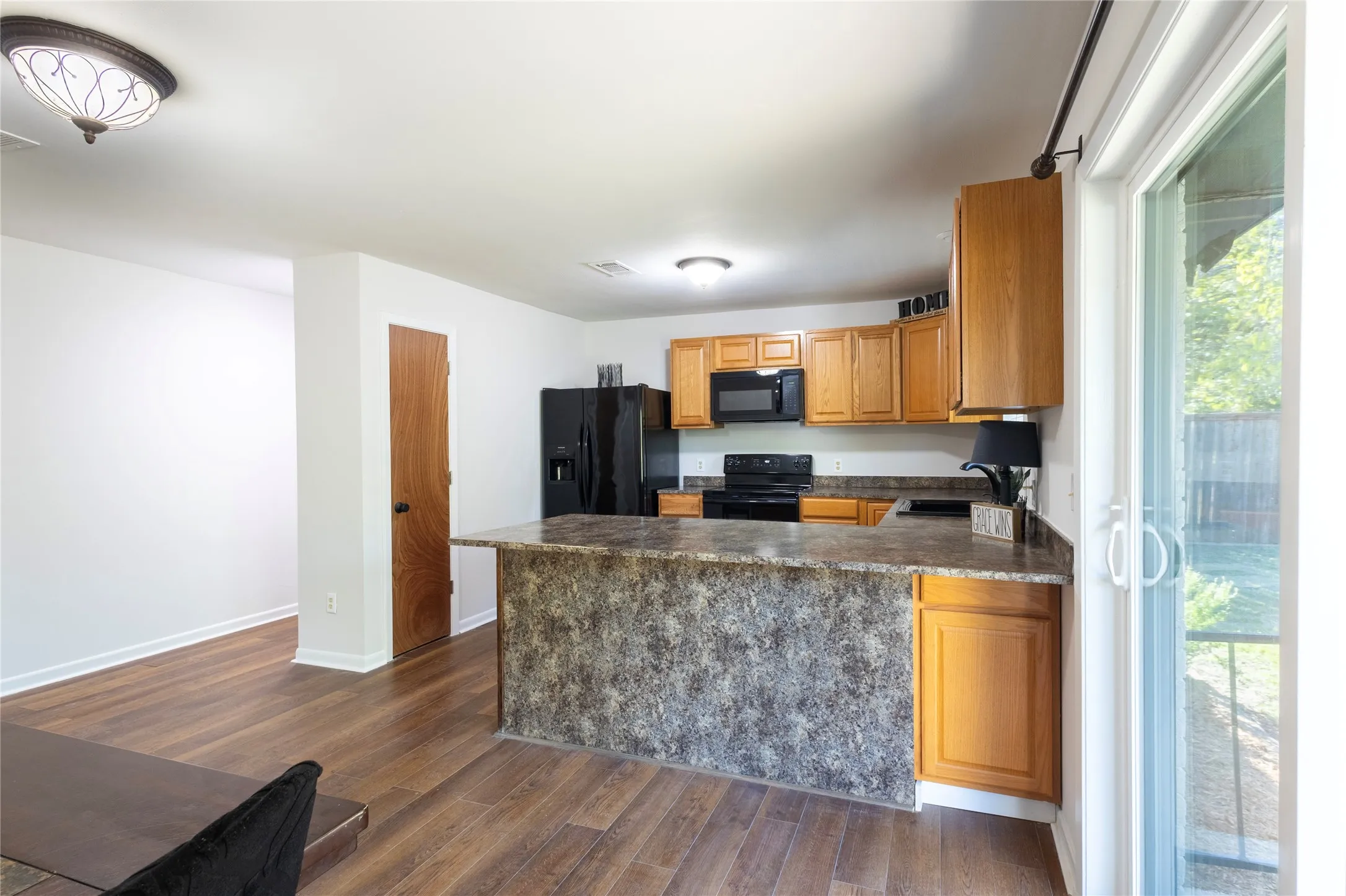 Kitchen featuring wood-finish cabinetry, stone-patterned countertops, a center island with bar seating, black appliances, and sliding glass doors