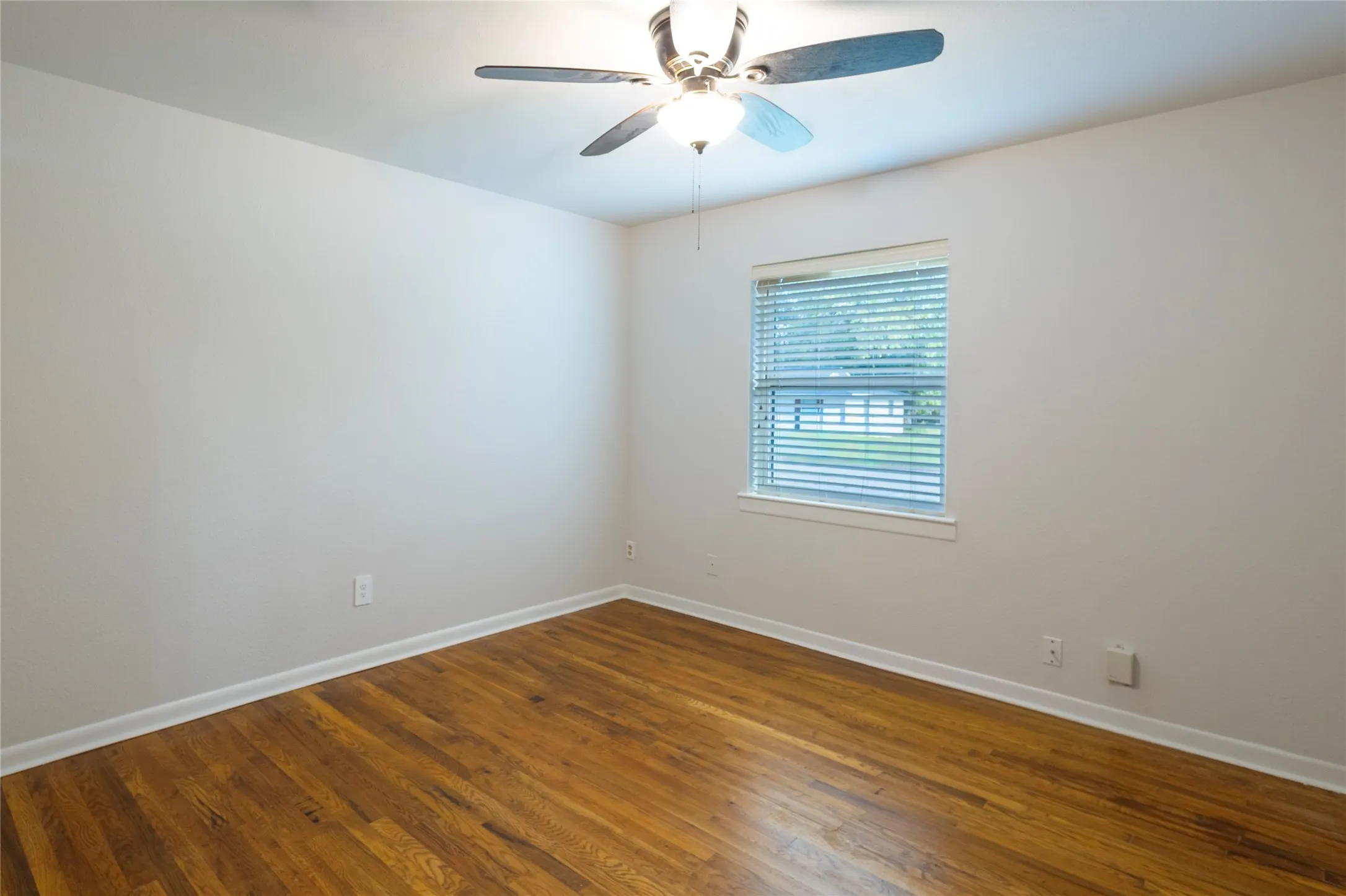 Room featuring wood-finish flooring, a multi-blade ceiling fan with integrated light fixture, and horizontal window blinds