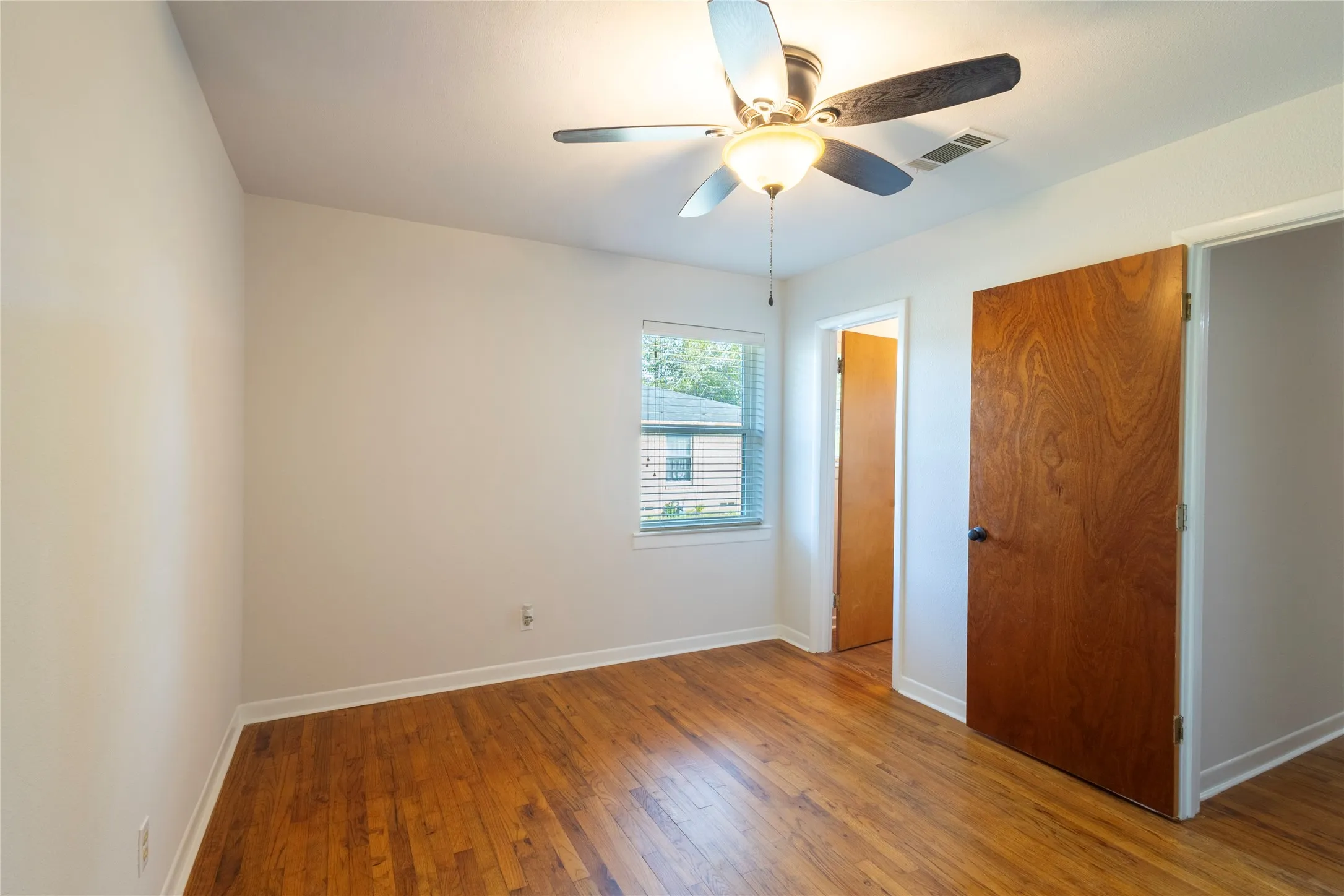 Wood-finish flooring, central ceiling fan with integrated lighting, and natural wood-grain interior door