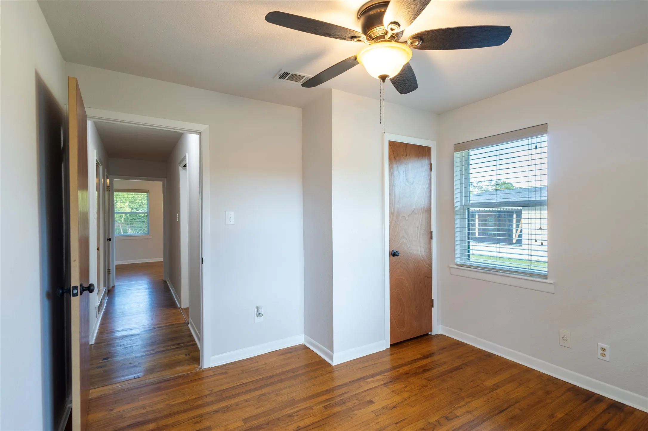 Room featuring wood-finish flooring, a ceiling fan with integrated lighting, and a single-panel wood door