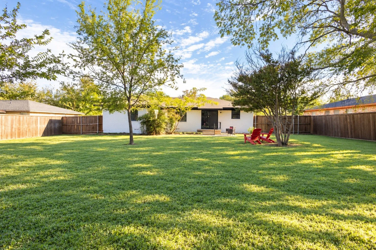 Expansive backyard featuring a large grass lawn, mature trees, and full perimeter wood fencing
