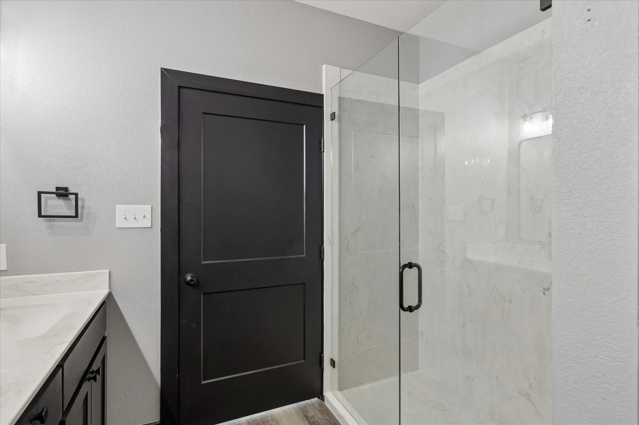 Walk-in shower with floor-to-ceiling surround and glass door, vanity with solid surface countertop, and black-finish door and hardware