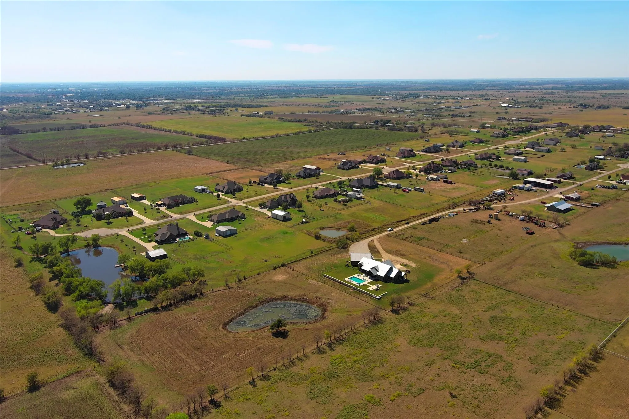 Aerial perspective of a sprawling rural property featuring a large residence, an inground pool, a private pond, and expansive open acreage