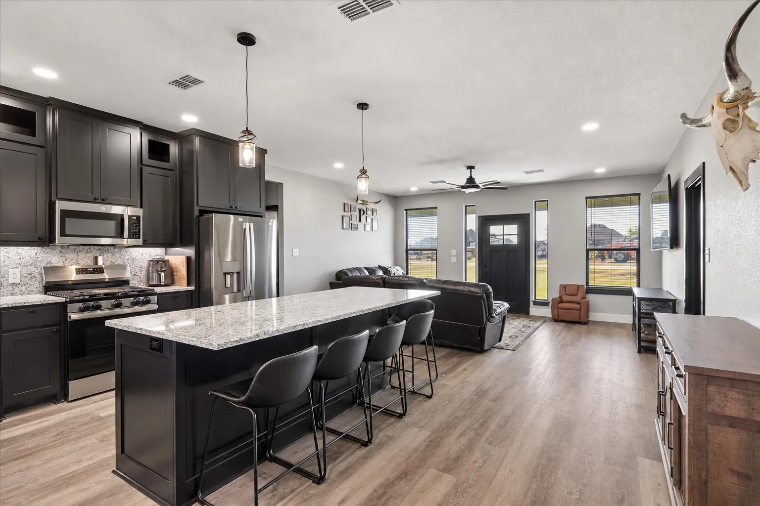Kitchen featuring dark cabinetry, expansive stone-finish countertops, stainless steel appliances, dual pendant lighting, and wood-finish flooring