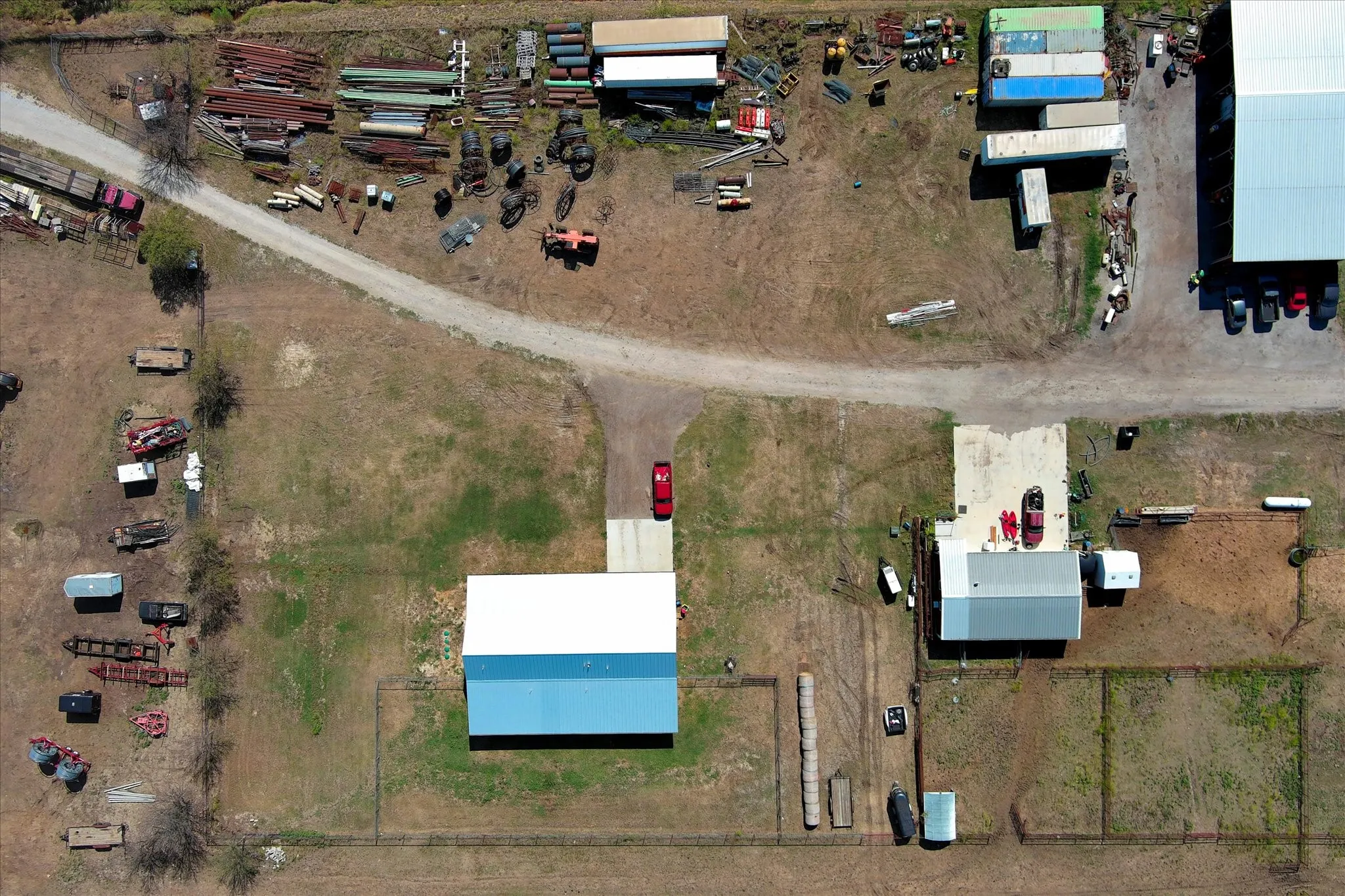 Aerial perspective of expansive acreage featuring multiple metal-roofed structures, gravel access paths, and fenced enclosures