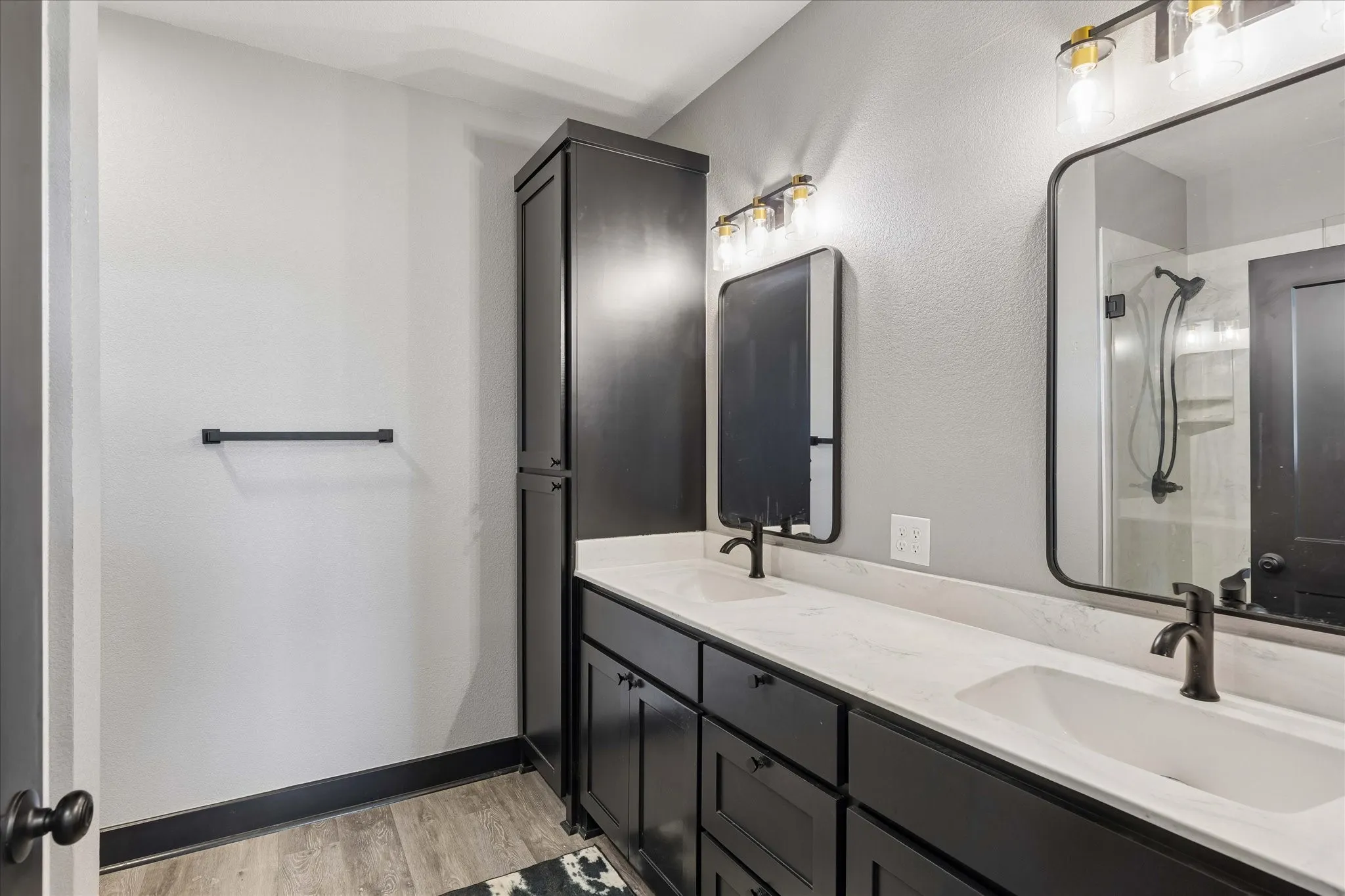 Dual-sink vanity featuring matte black hardware, stone-composite countertop, floor-to-ceiling built-in cabinetry, and rectangular mirrors with black frames