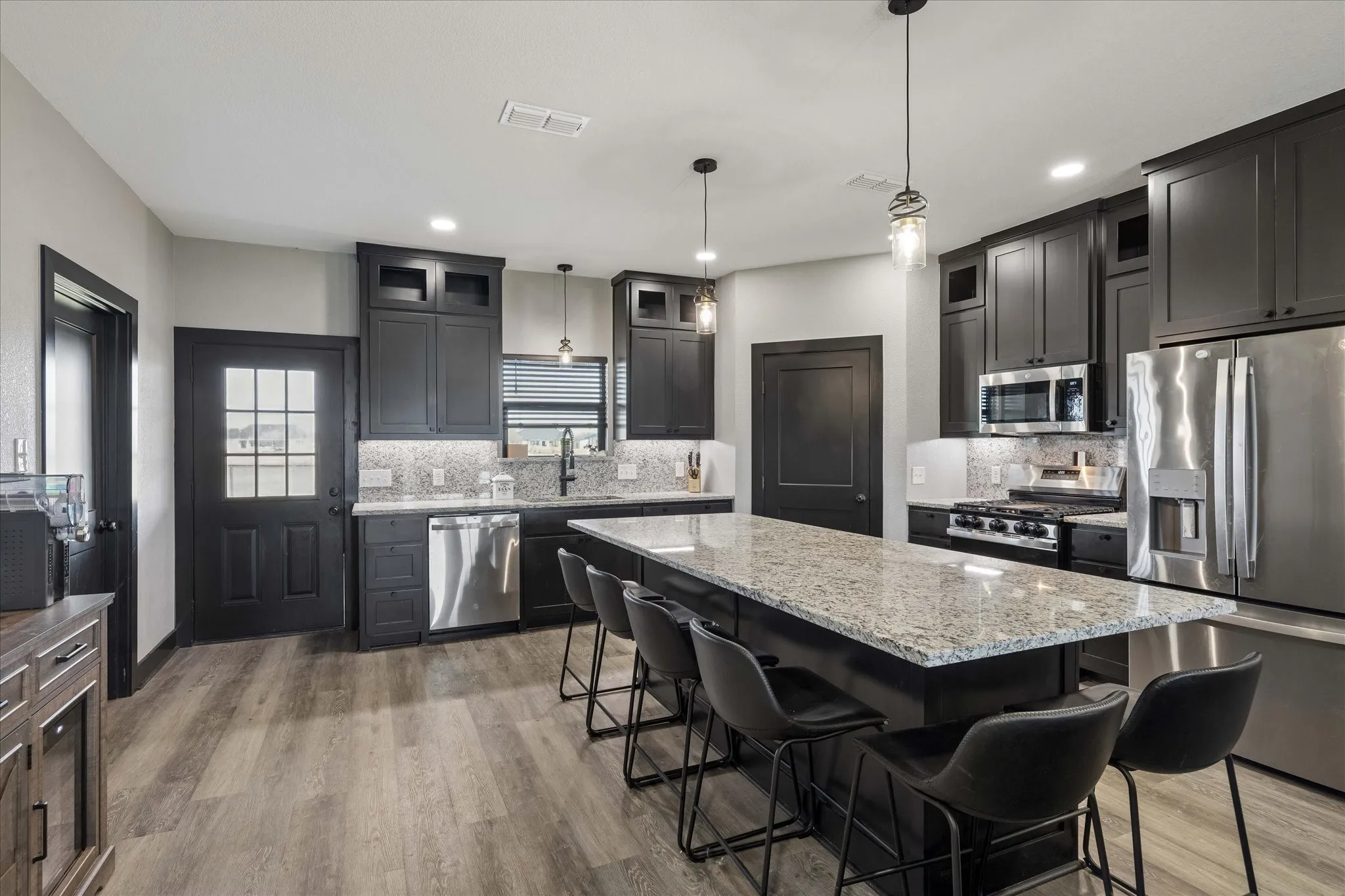 Kitchen featuring dark cabinetry, expansive stone-surface center island, stainless steel appliances, and wood-finish flooring