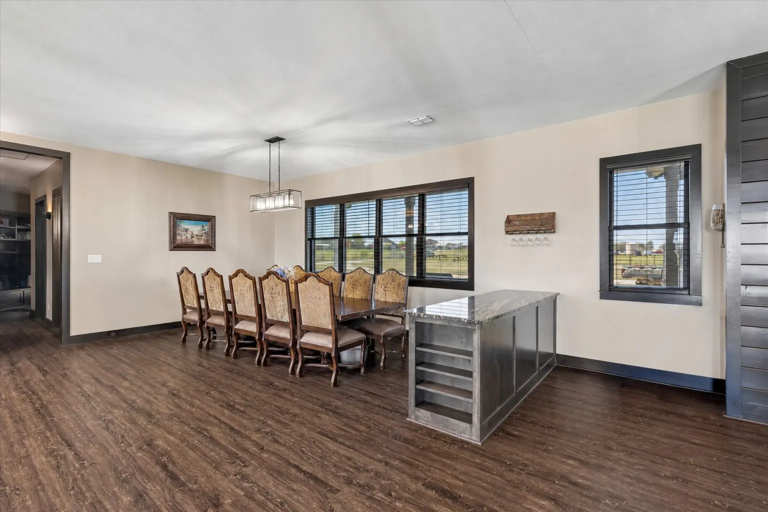 Dining area featuring dark wood-finish flooring, built-in stone-top cabinetry with integrated shelving, a multi-light linear chandelier, and dark-trimmed windows