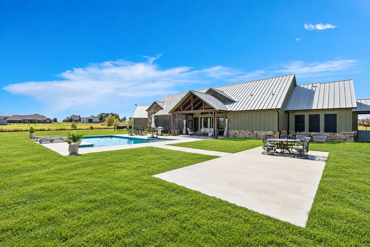 Expansive backyard featuring a covered patio with timber framing, an in-ground swimming pool, stone exterior accents, and a metal roof