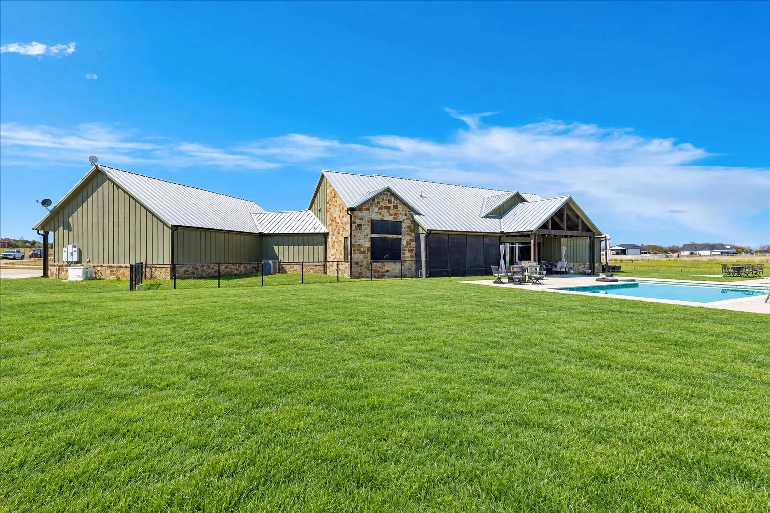Exterior featuring metal roofing, vertical siding, stone masonry, a covered porch, and an inground swimming pool set in an expansive lawn