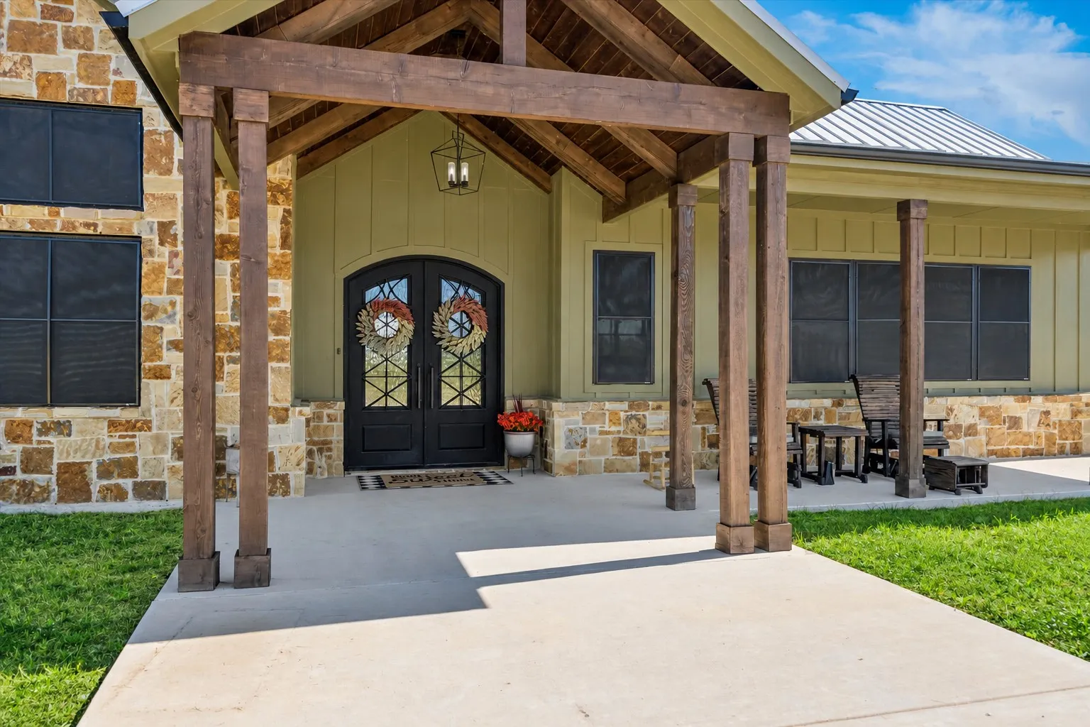 Exterior entrance featuring stacked stone masonry, a timber-framed gabled portico, double doors with glass detailing, and a metal roof