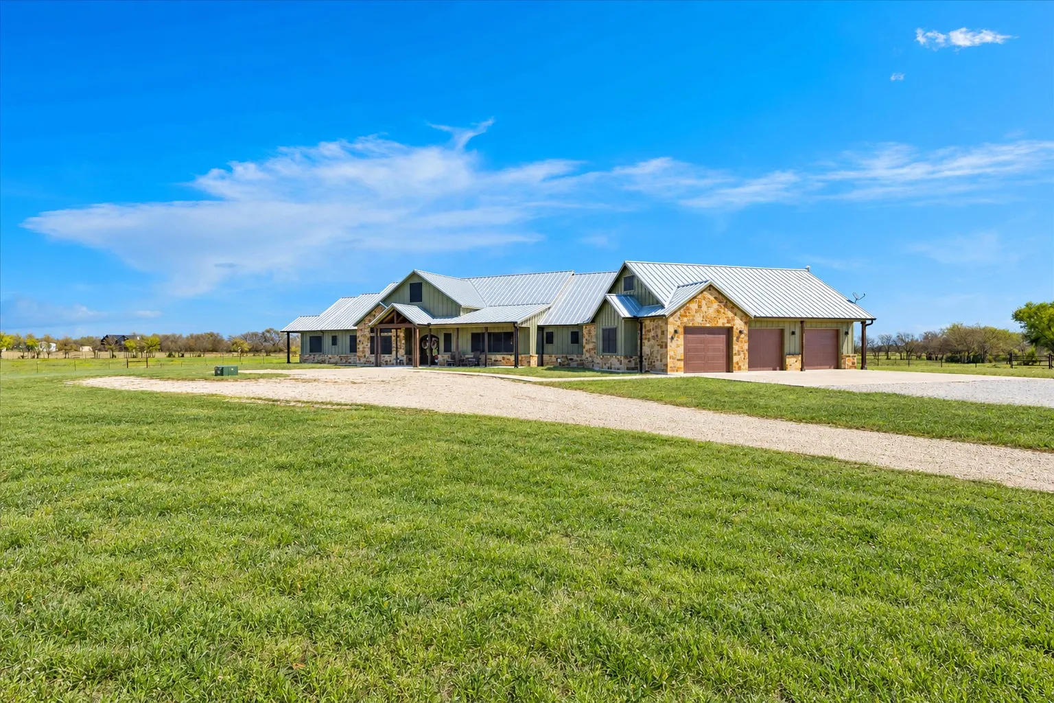 Single-story exterior featuring stone and siding finishes, a metal roof, three-car garage, and expansive acreage