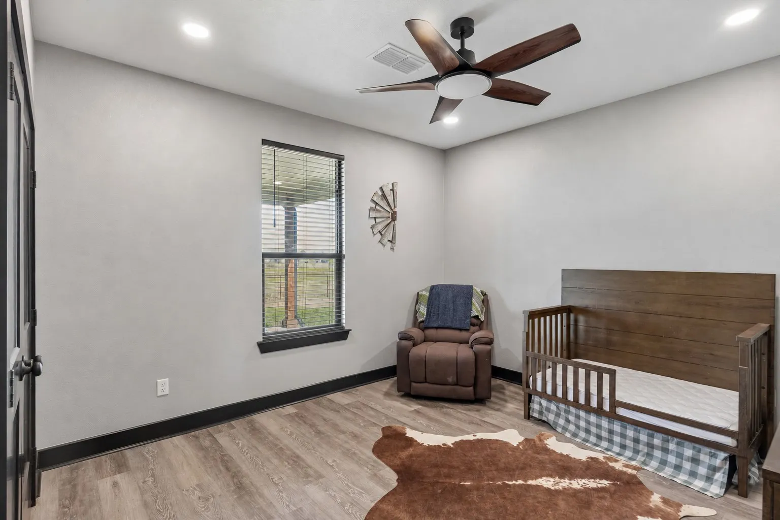 Neutral-toned room featuring wood-finish flooring, recessed lighting, a modern ceiling fan with integrated light fixture, and a single-pane window with dark trim