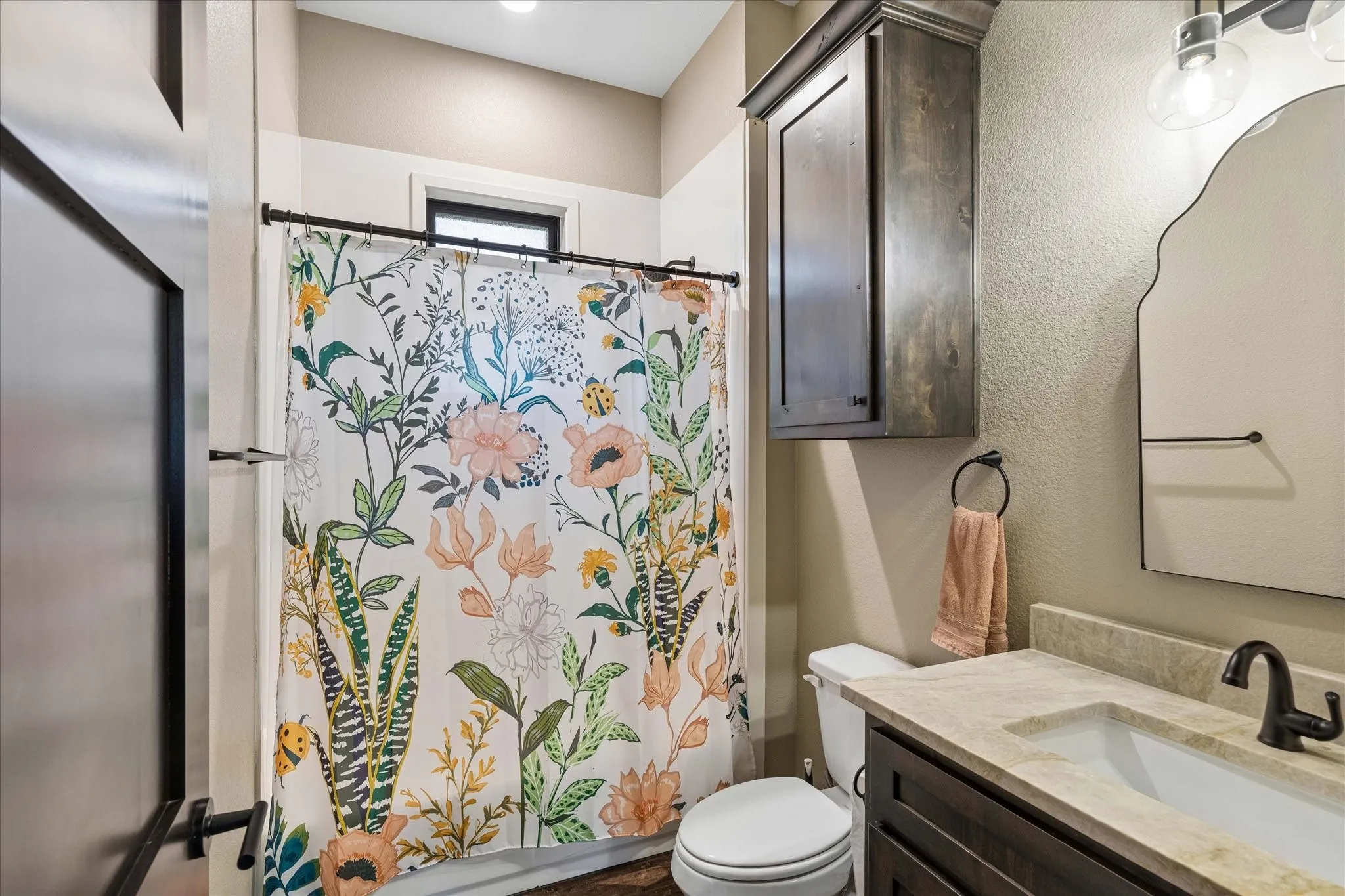 Bathroom featuring dark wood-finish cabinetry, a stone-composite countertop with an integrated basin, a wall-mounted medicine cabinet, a decorative arched mirror, and a matte black faucet