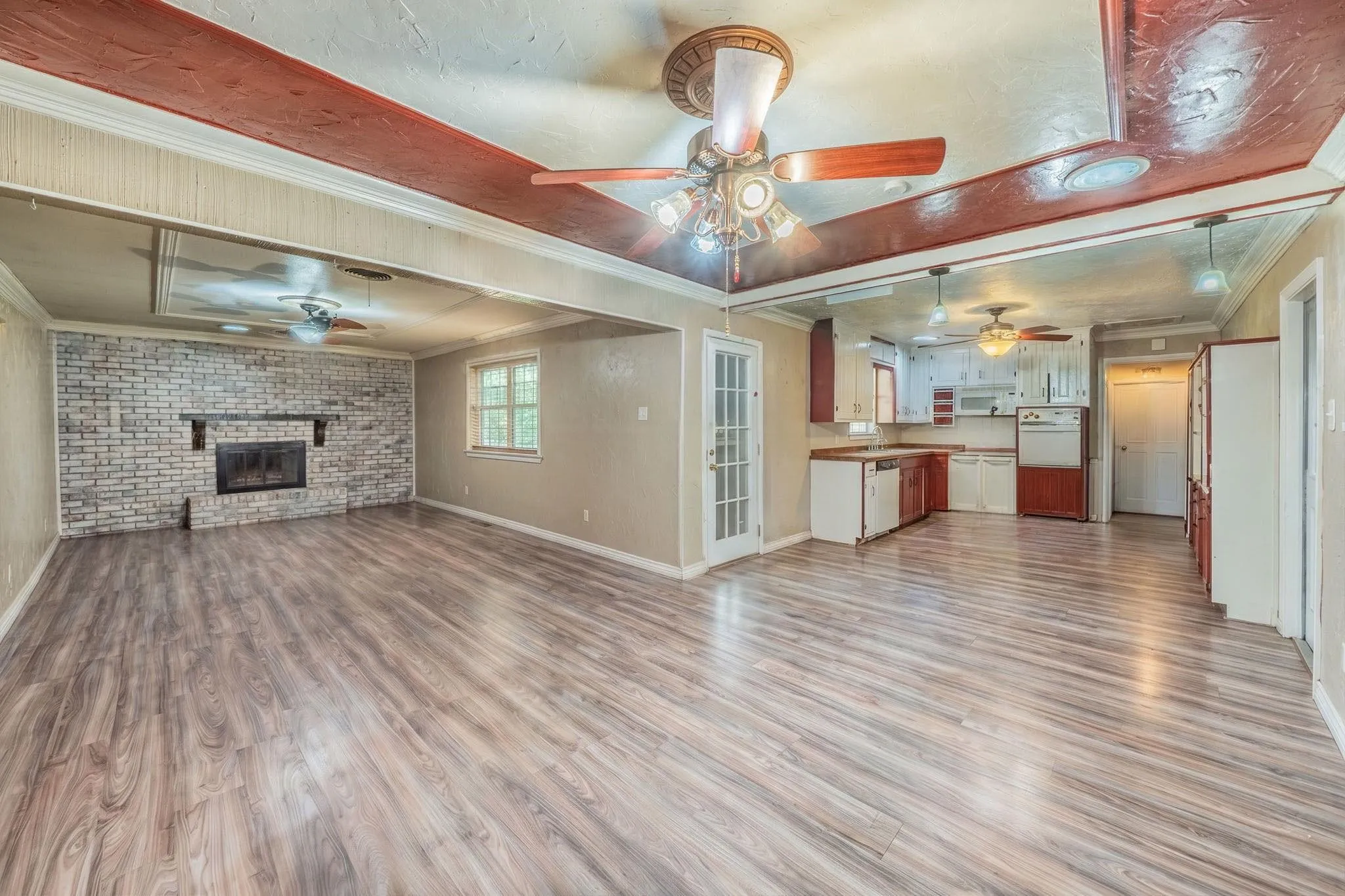 Open living area featuring wood-finish flooring, a tray ceiling with recessed wood detailing, and a floor-to-ceiling brick fireplace