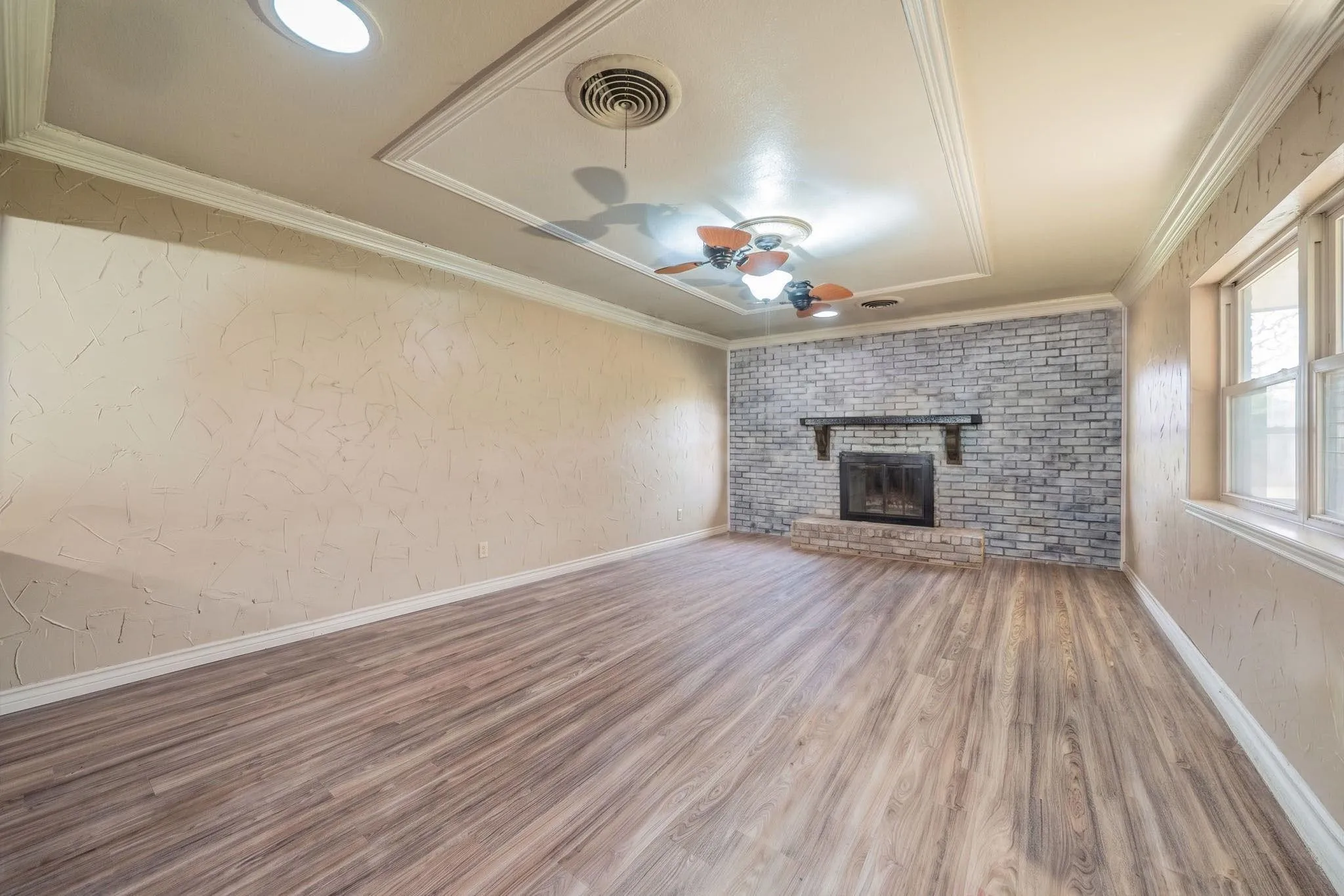 Interior space featuring wood-finish flooring, a tray ceiling with crown molding, and a gray painted brick fireplace with a custom mantel