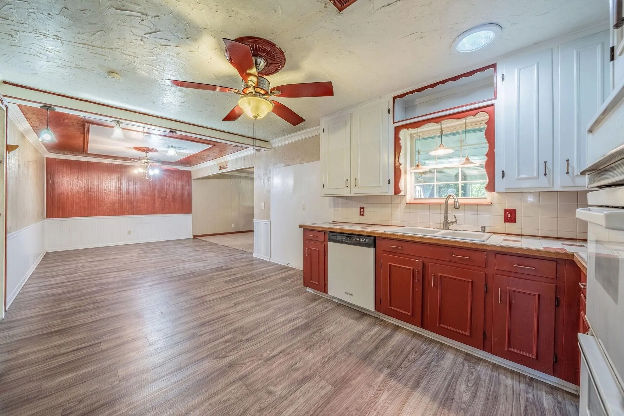 Kitchen featuring white upper cabinetry, red lower cabinetry, a built-in dishwasher, a double-basin sink with a gooseneck faucet, and wood-finish flooring