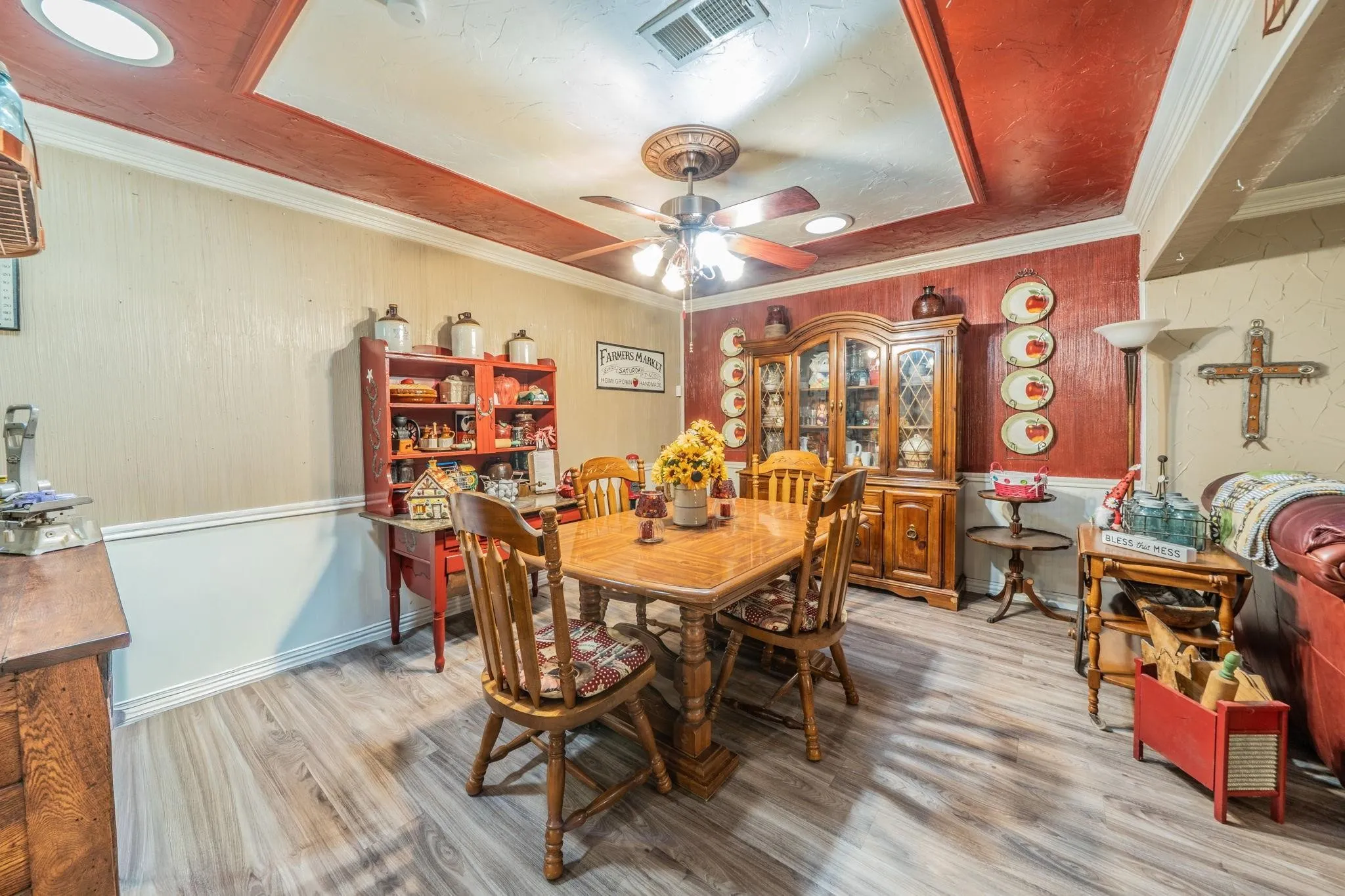 Wood-finish flooring, tray ceiling with decorative molding, and central ceiling fan with multi-light fixture