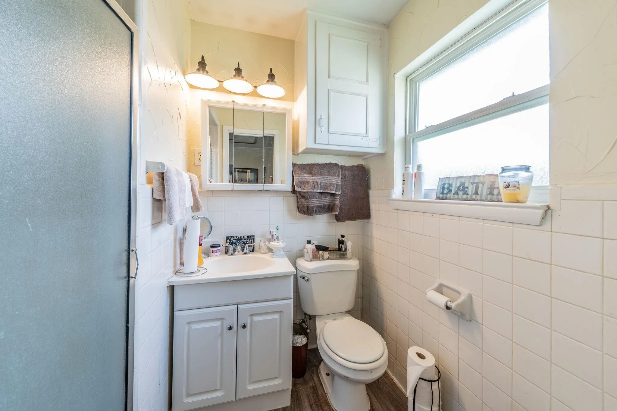 Bathroom featuring a vanity with integrated sink, three-light fixture, medicine cabinet, upper storage cabinetry, and tiled wall surround