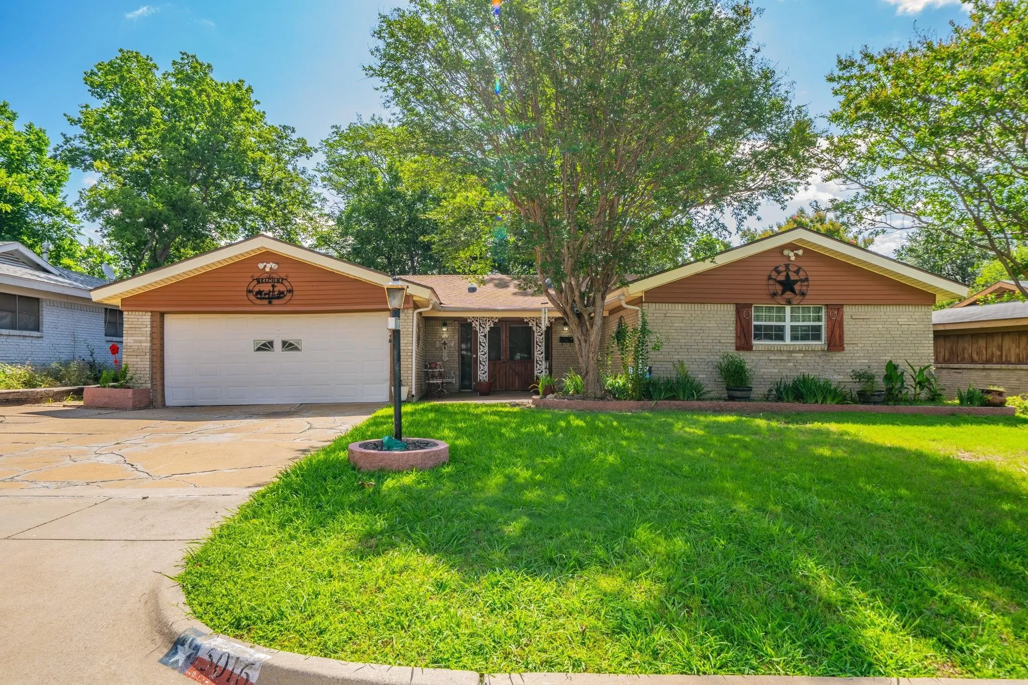 Single-story residence featuring a brick and horizontal siding exterior, a two-car attached garage, and a landscaped front lawn with mature trees