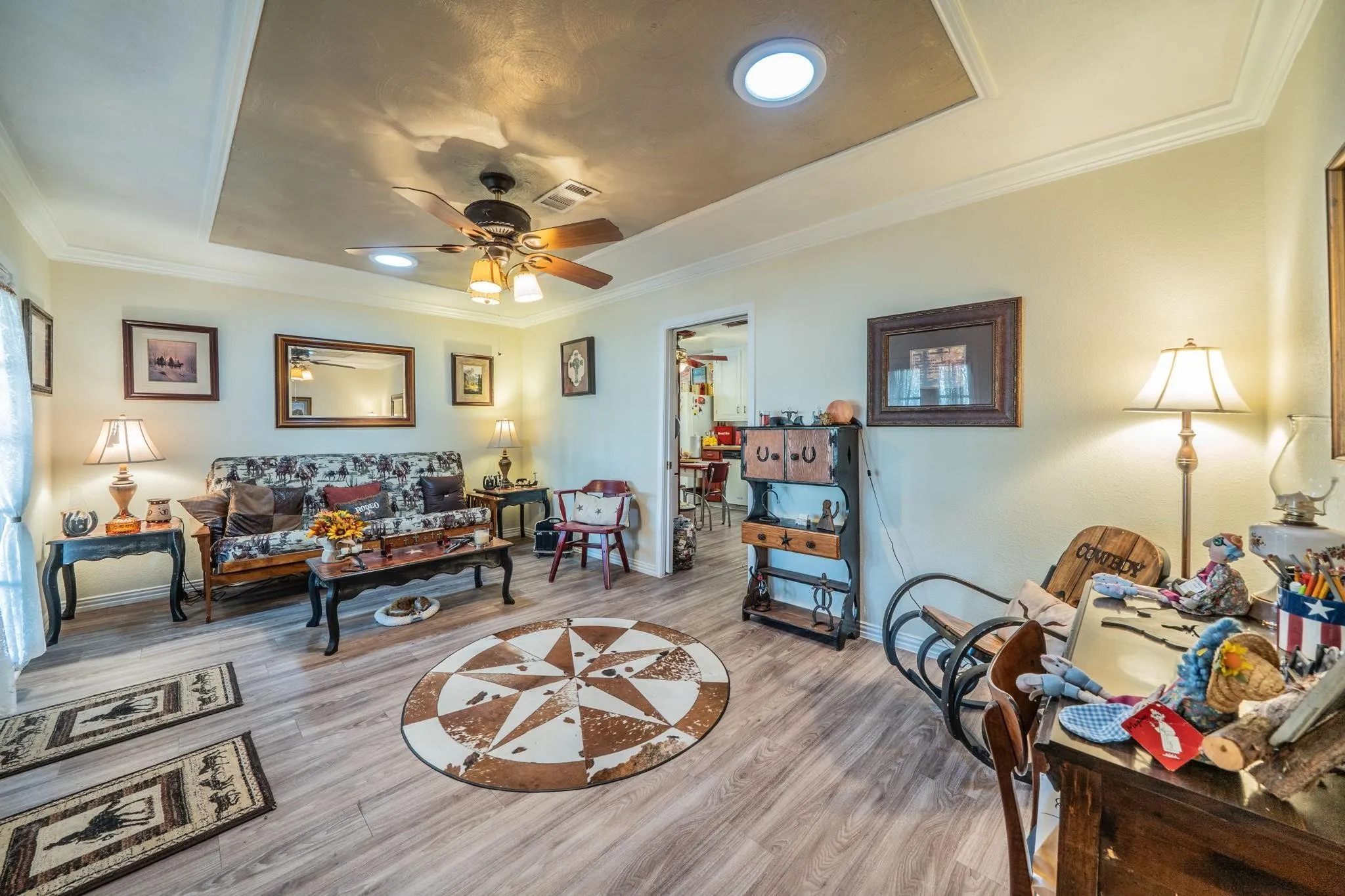 Living area featuring a recessed tray ceiling, wood-finish flooring, two circular skylights, and a central ceiling fan with integrated lighting