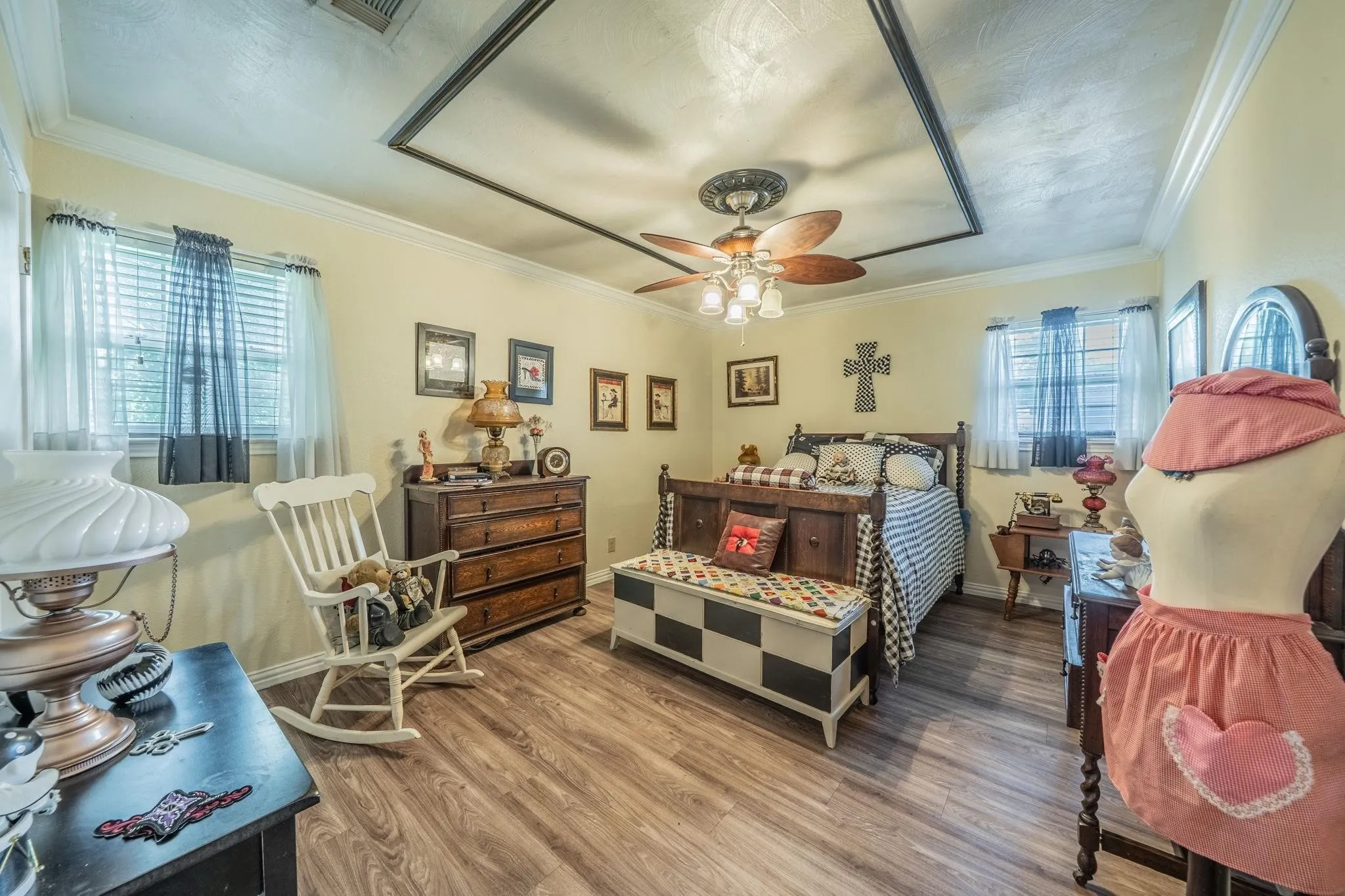 Wood-finish flooring, recessed ceiling accent detail, multi-blade ceiling fan with integrated lighting, crown molding, and dual windows with window treatments
