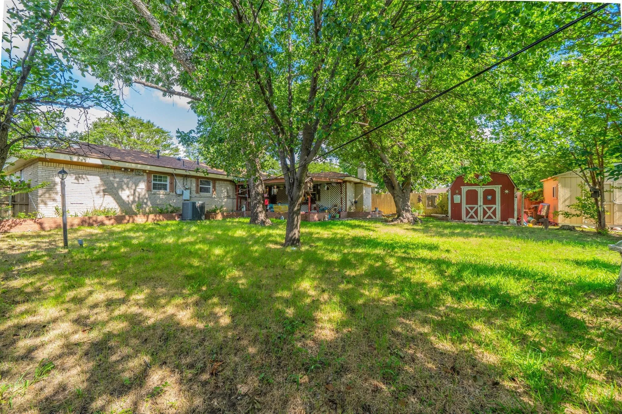 Expansive backyard featuring mature shade trees, a brick exterior residence, and two detached storage structures